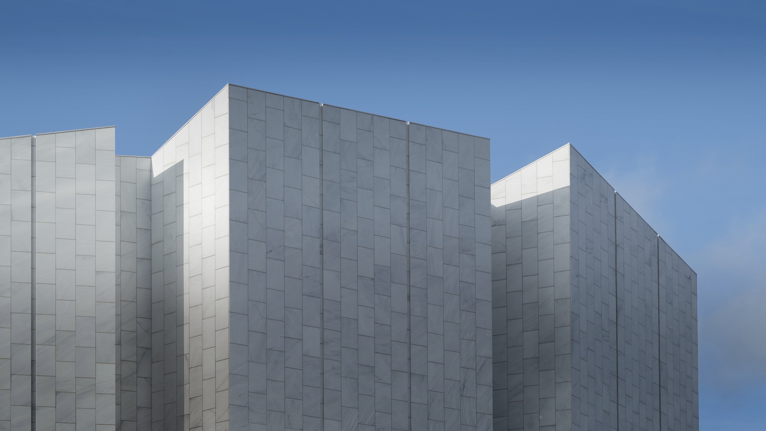 Modern building facade with rectangular white tiles and clear blue sky in the background.