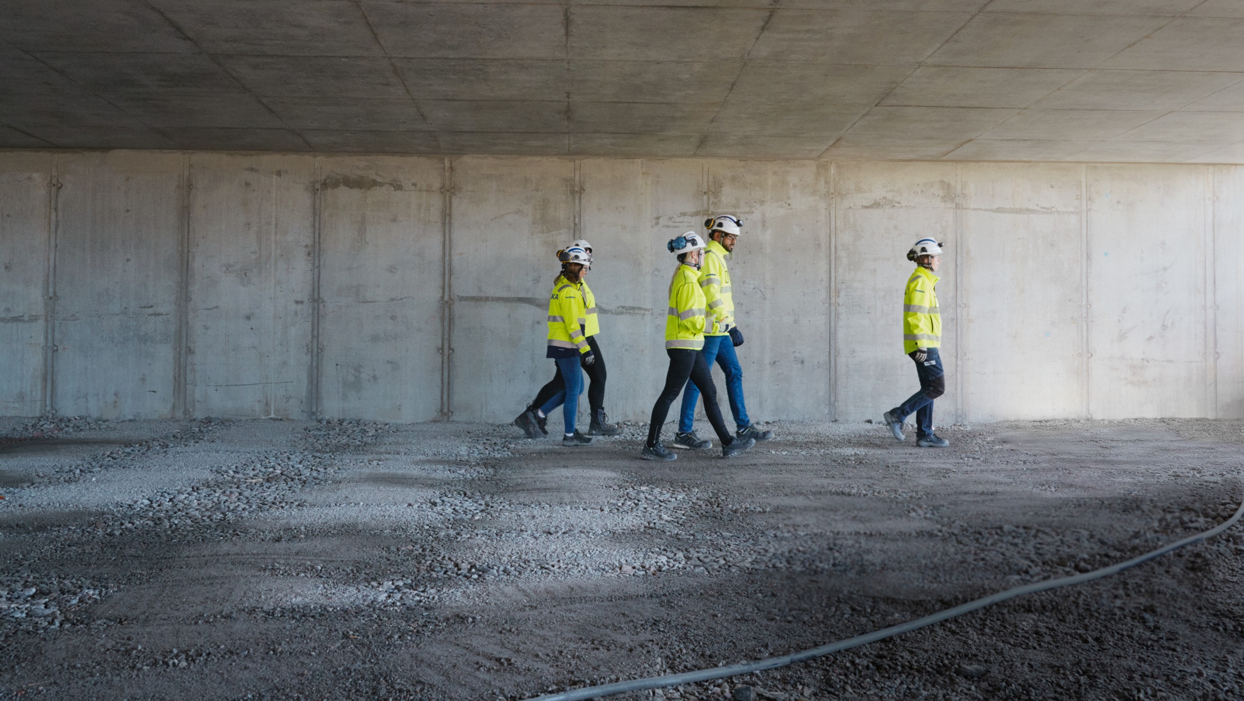 Four construction workers in safety gear walking inside a concrete structure under construction.