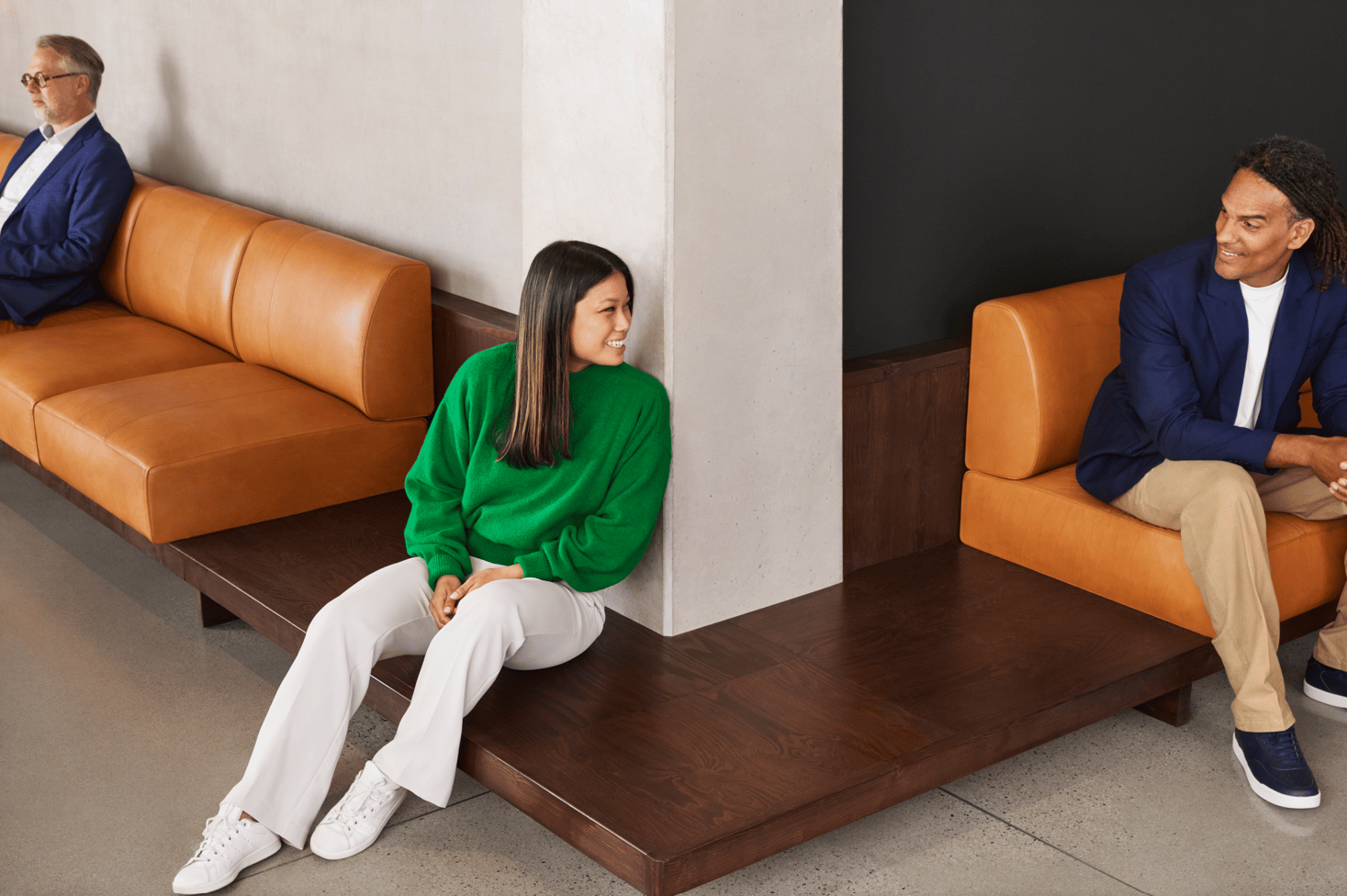 Tre olika personer som sitter åtskilda på moderna bruna lädersoffor i en stilfull lobby.