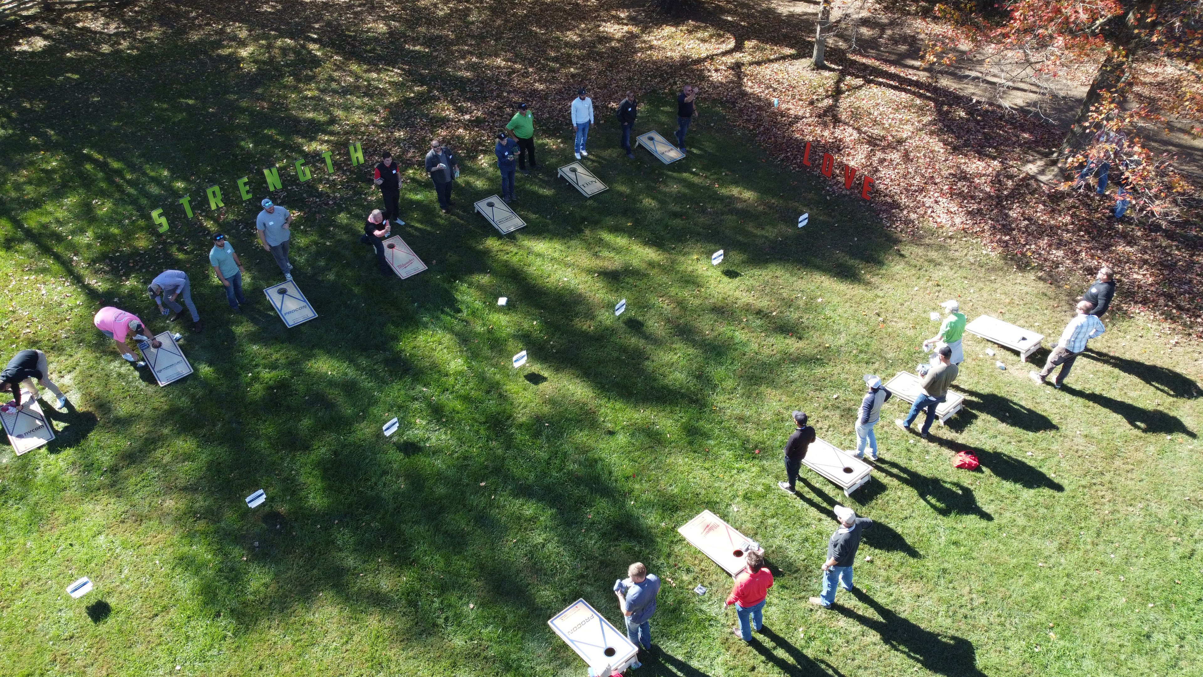 Outdoor Team Building Activity with Strength and Love Themes People playing cornhole outdoors on grass under sunlight with shadows and autumn trees.