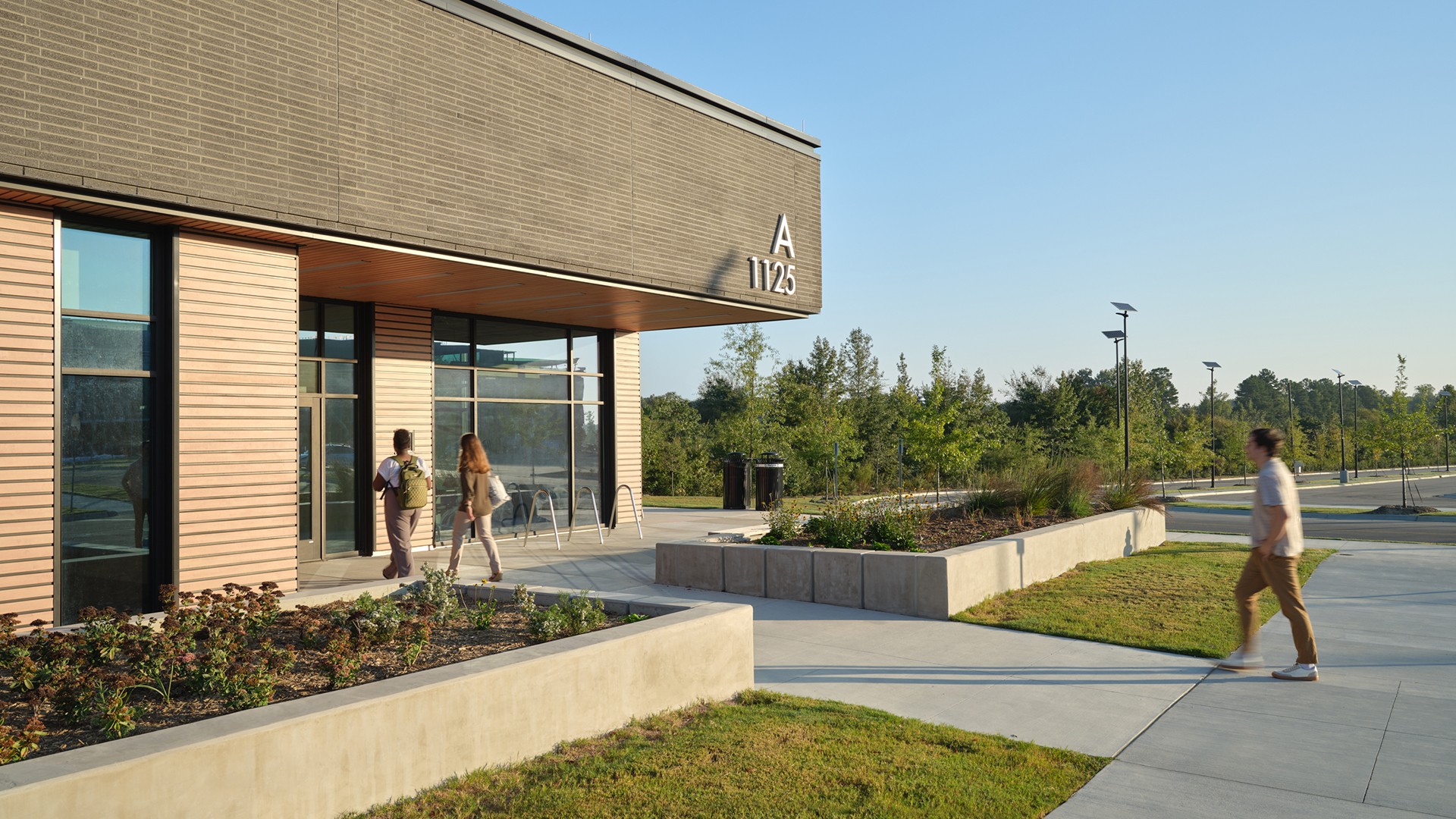 Modern campus building entrance with students walking nearby Modern school building entrance with students walking on a sunny day and greenery.