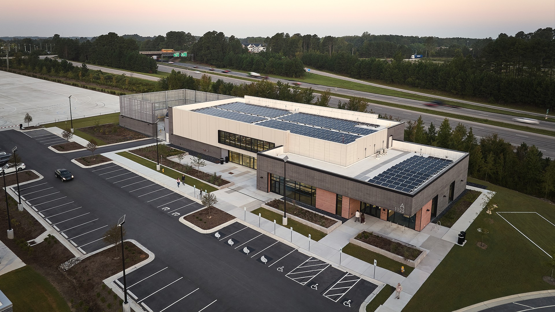 Modern Building with Solar Panels Near Highway and Parking Lot Modern building with solar panels on the roof and adjacent empty parking lot near highway.