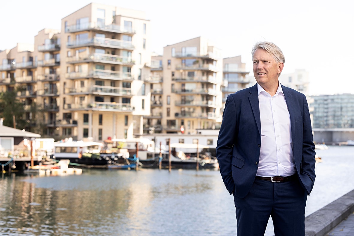 Businessman in navy suit standing by urban waterfront on sunny day Businessman in navy suit standing by waterfront with modern apartments in background.