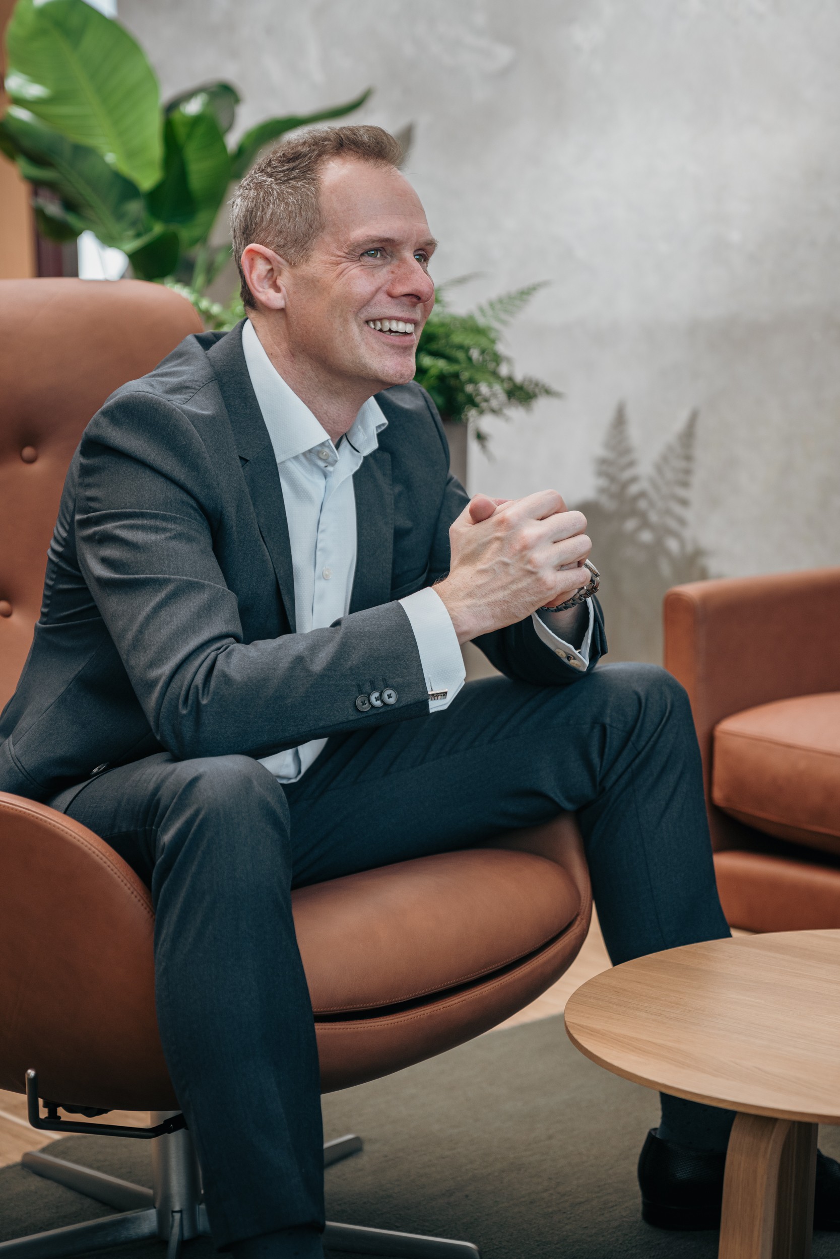 Businessman in suit sitting thoughtfully in modern office chair Man in business suit sitting thoughtfully in modern office chair beside wooden table.