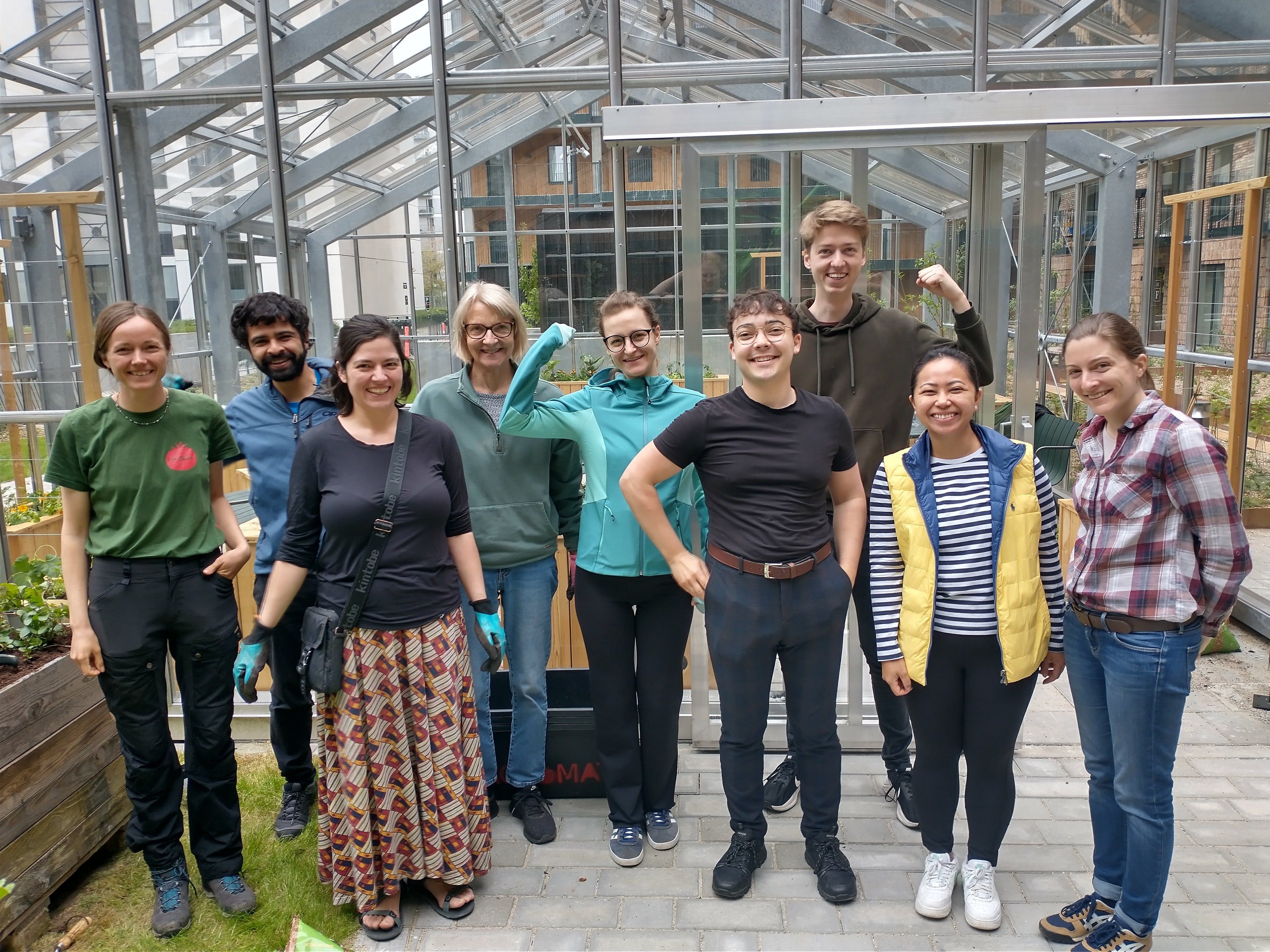 Group of diverse young adults posing confidently in a greenhouse setting, smiling.