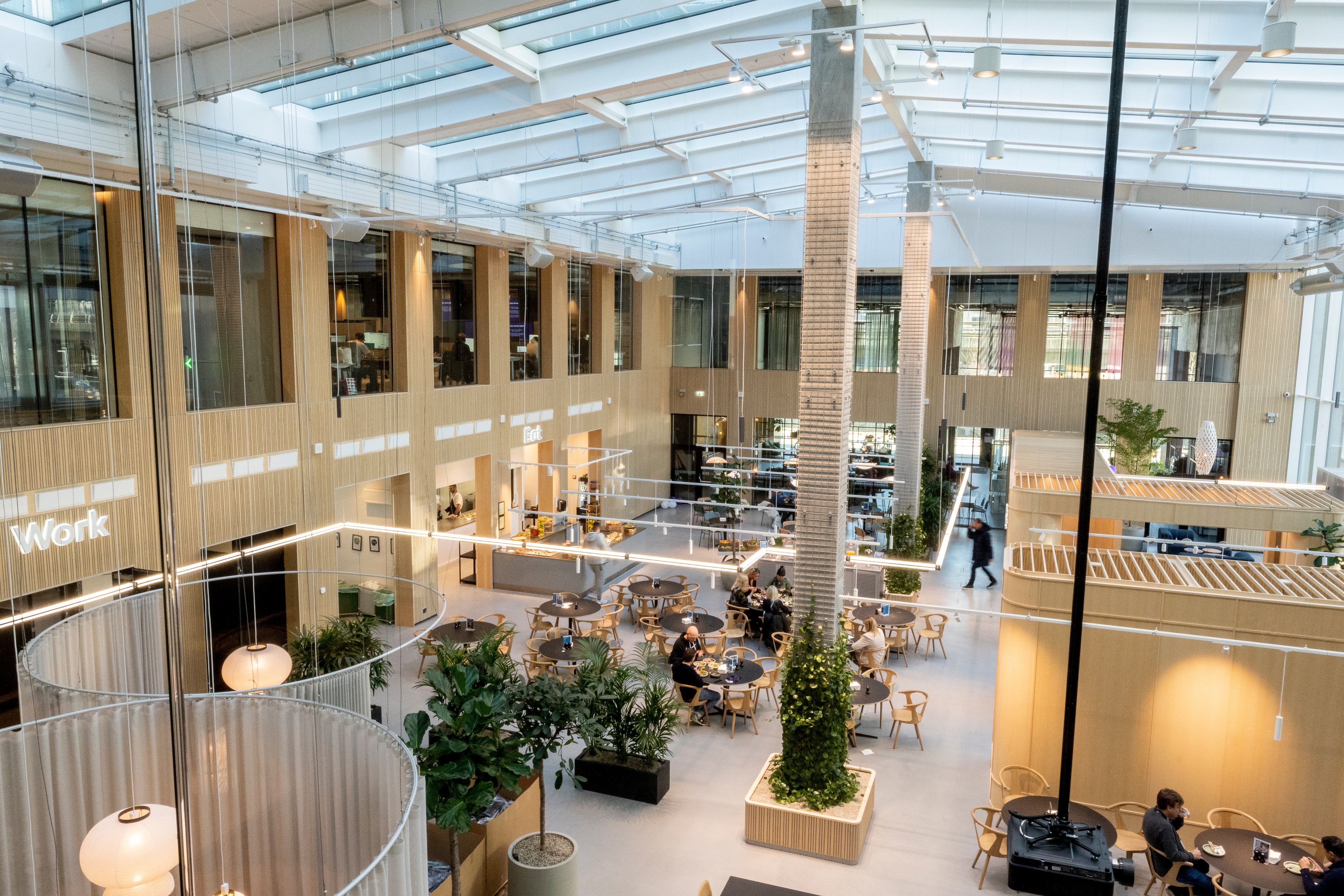 Modern coworking space with natural light, plants, and people working at tables.