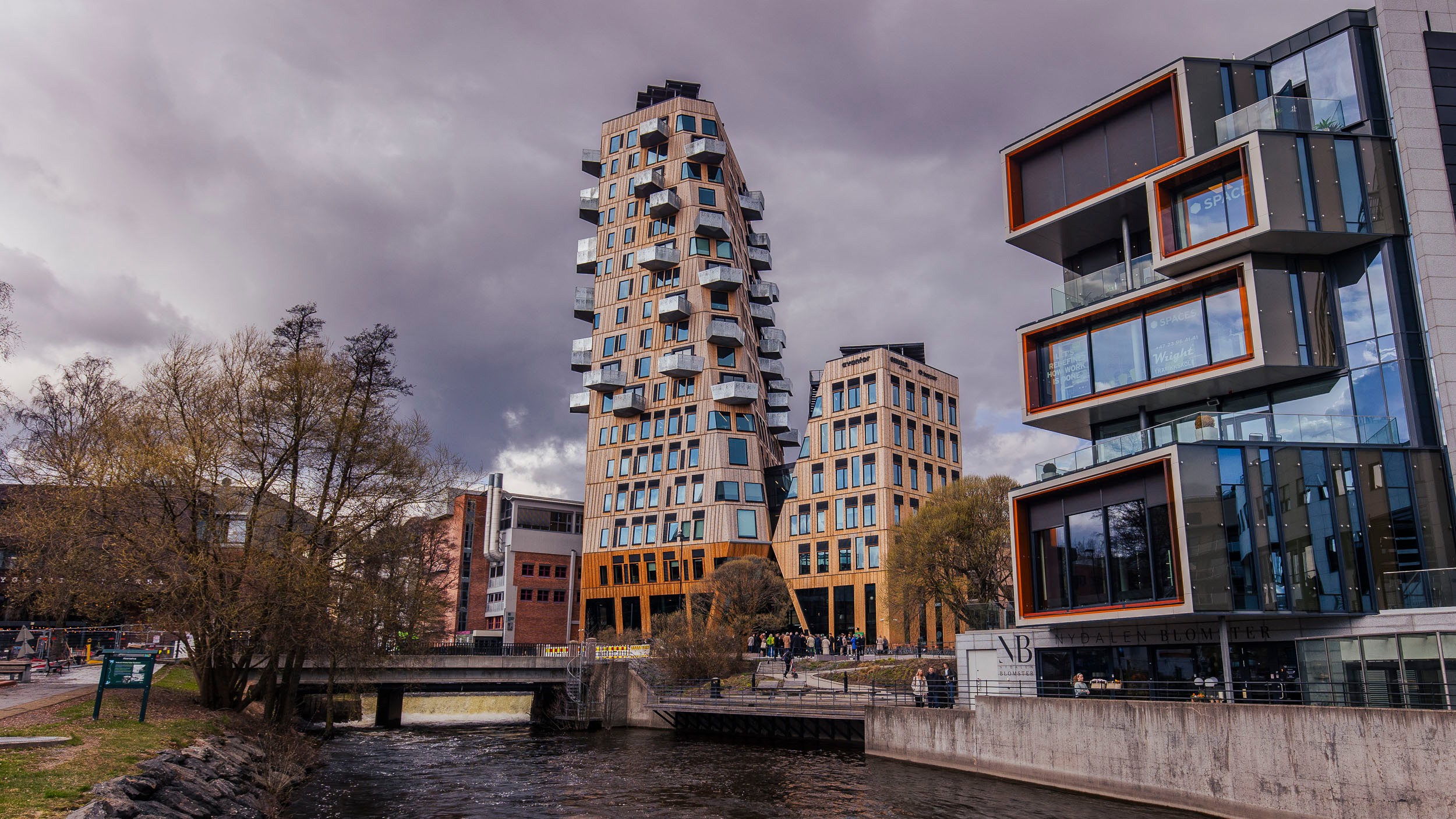 Modern high-rise buildings by a river under a cloudy sky in an urban setting.