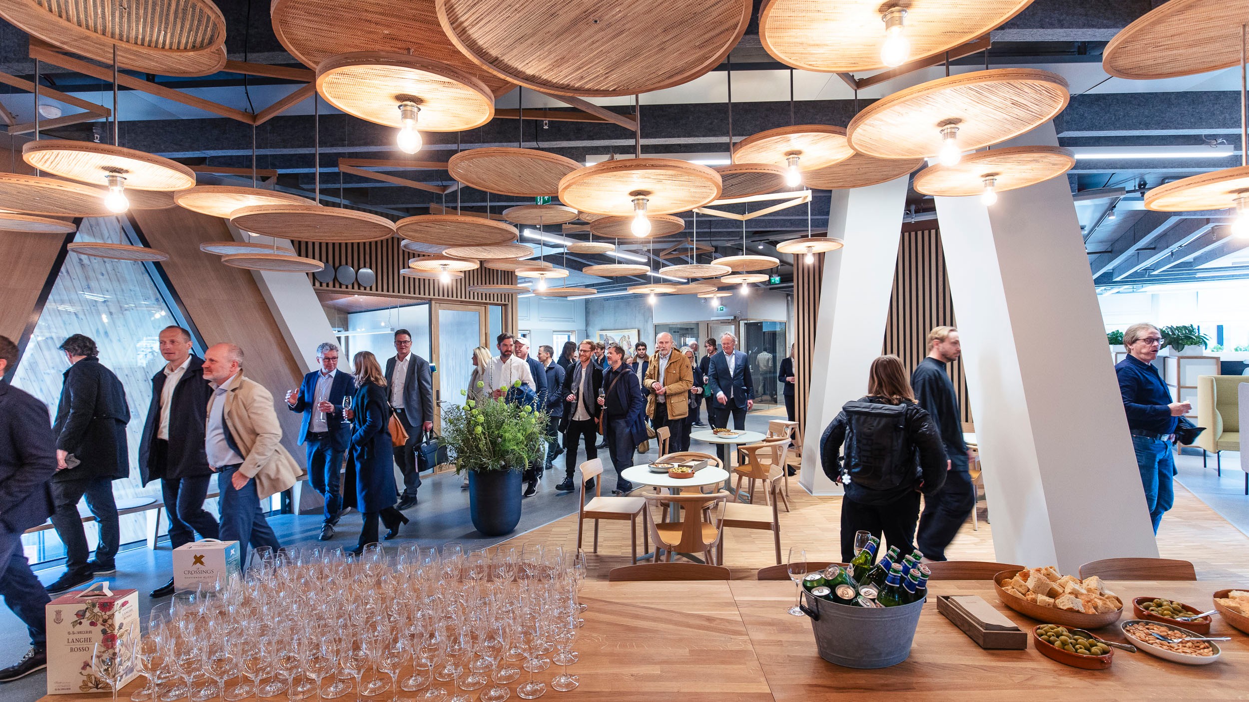 People walking through a modern, well-lit event space with wooden decor and refreshments.