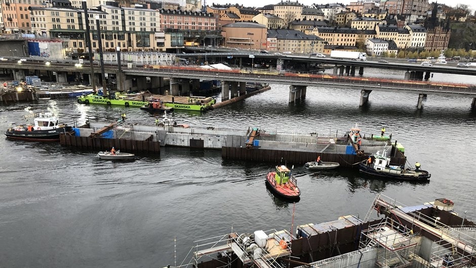 Byggpråmar och bogserbåtar som arbetar på ett kajprojekt nära stadens broar.