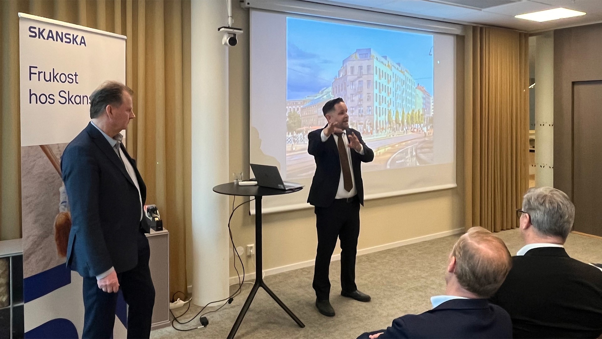 Business professionals attending a Skanska breakfast presentation in a conference room.