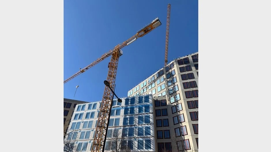 Byggkranar som reser sig över moderna glas- och betongkontorsbyggnader under klar himmel.