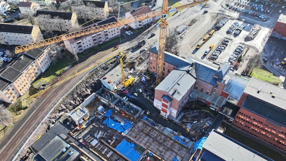 Flygfoto av en urban byggarbetsplats med kranar och omgivande byggnader.