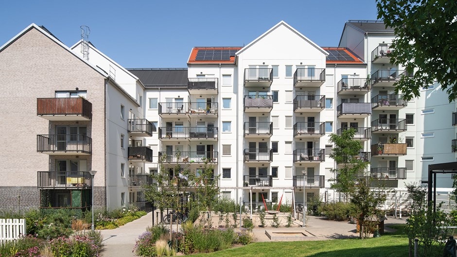Modern lägenhetskomplex med balkonger, solpaneler och en anlagd innergård.