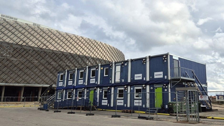 Staplade blåa portabla kontorscontainrar med trappor utanför en stor kupolbyggnad.