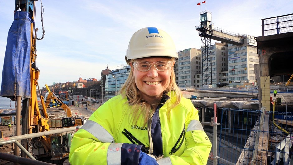 Byggnadsarbetare i högsynlighetsjacka och hjälm på byggarbetsplats i stadsmiljö.
