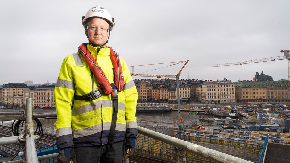 Byggnadsarbetare i högsynlighetsjacka och hjälm på byggarbetsplats i stadsmiljö.