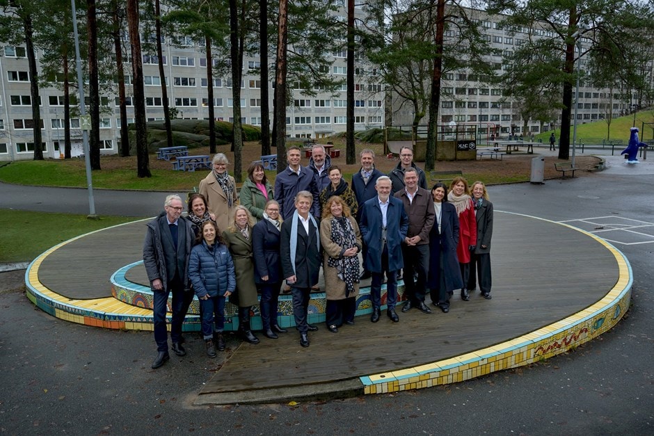 Grupp av olika vuxna som poserar utomhus på en cirkulär kaklad plattform i en stadspark.
