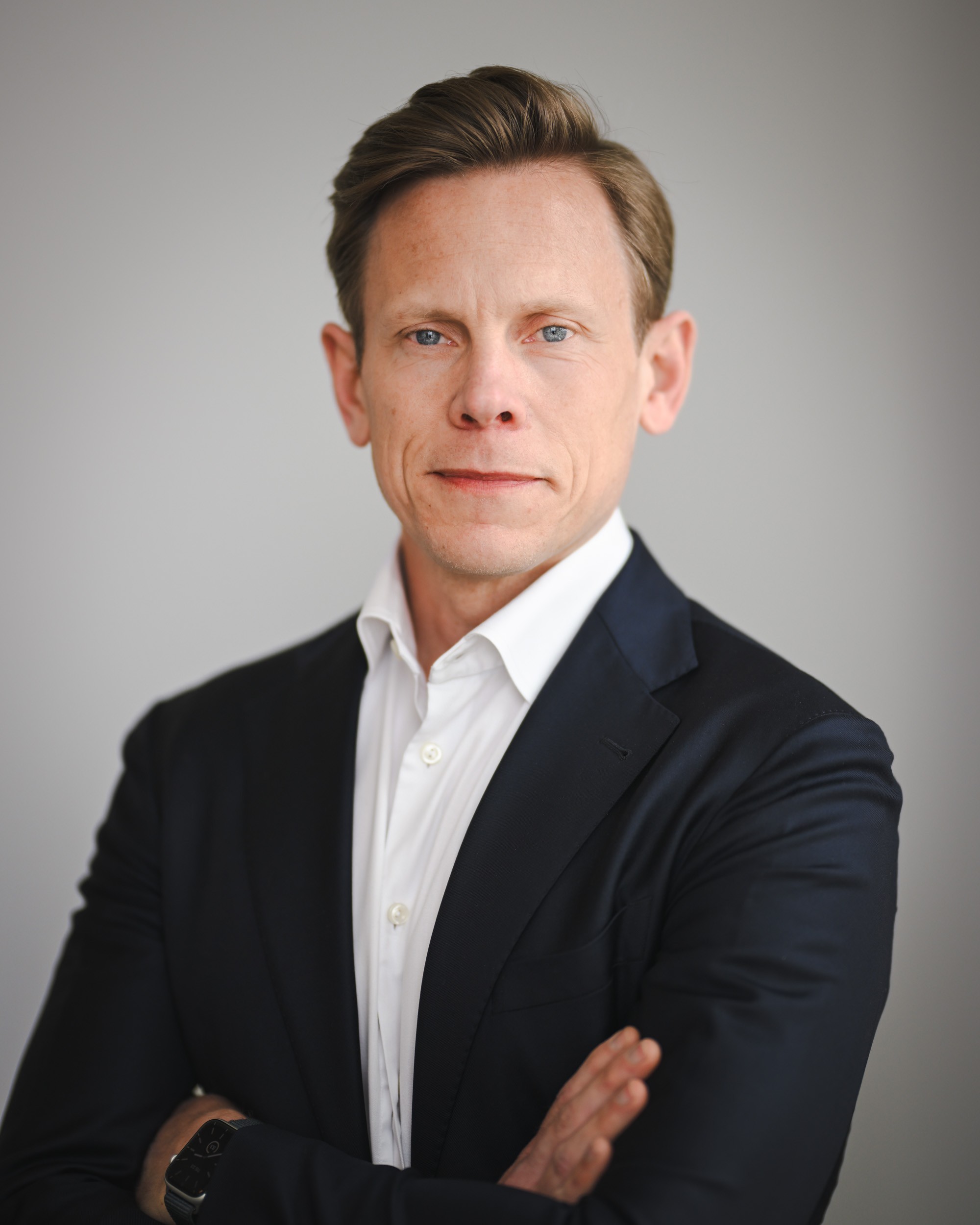 Professional Male in Business Attire with Crossed Arms A man in a dark suit with crossed arms and a white dress shirt, exuding professionalism.