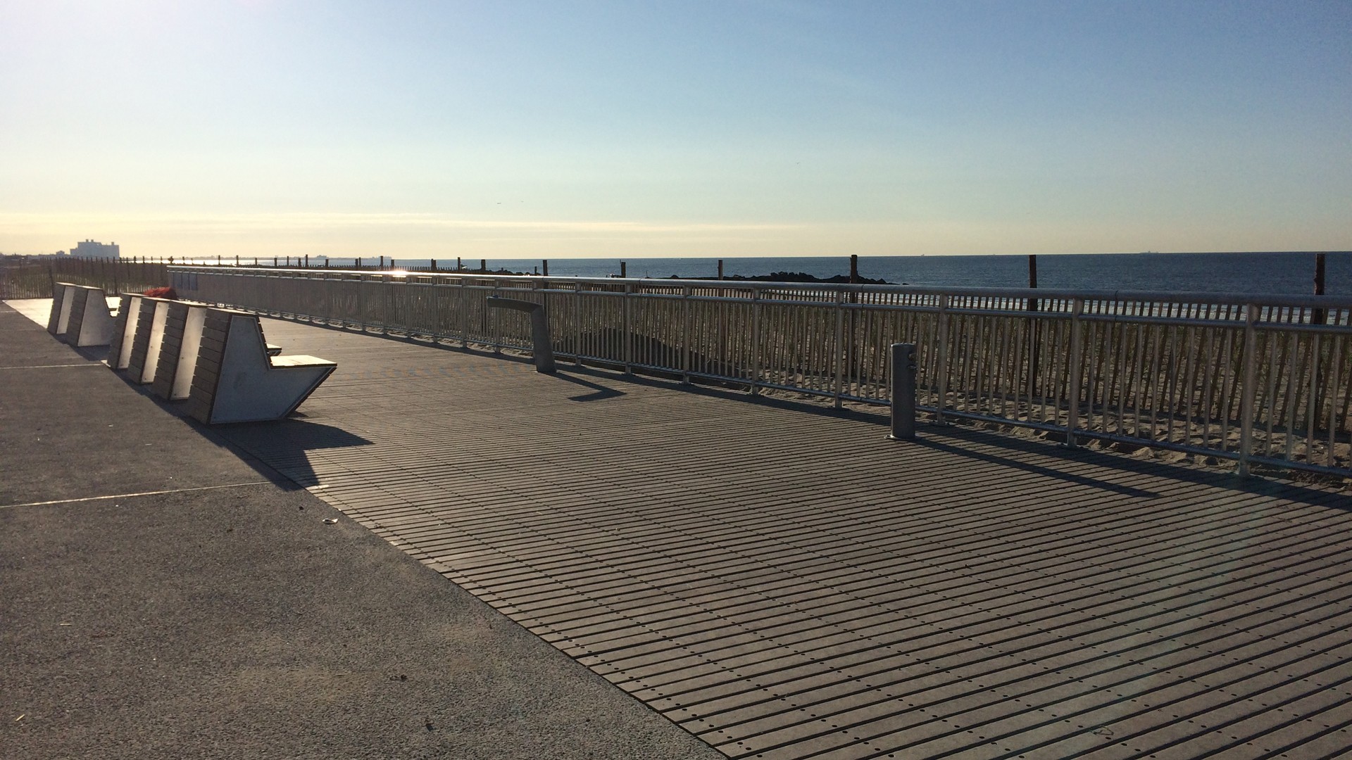 Sunny Oceanfront Boardwalk with Modern Seating Sunny beachfront boardwalk with modern benches and ocean view under clear blue sky.