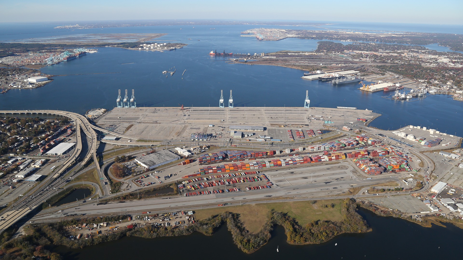 Aerial view of a large industrial port with shipping containers and cranes by the water.