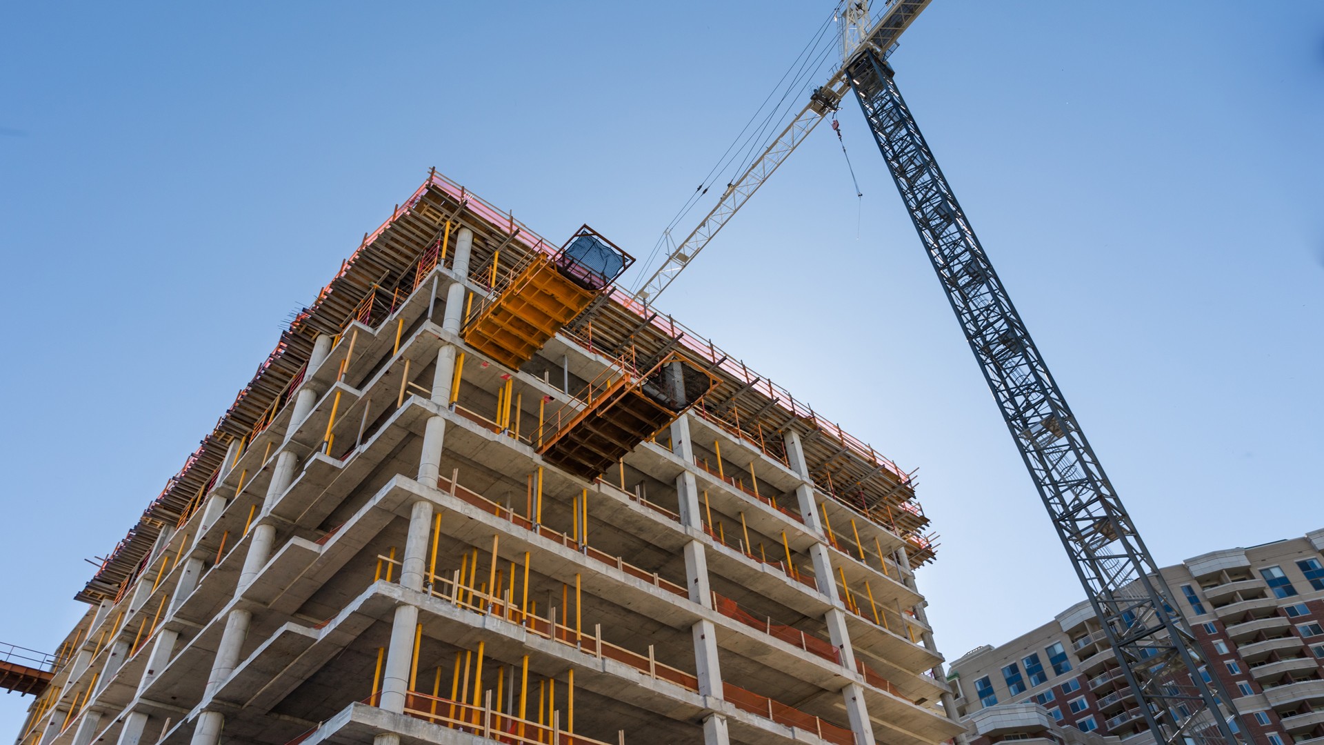 Urban Construction Site with Crane and Building Framework Construction site with crane lifting materials to an unfinished multi-story building under clear sky.