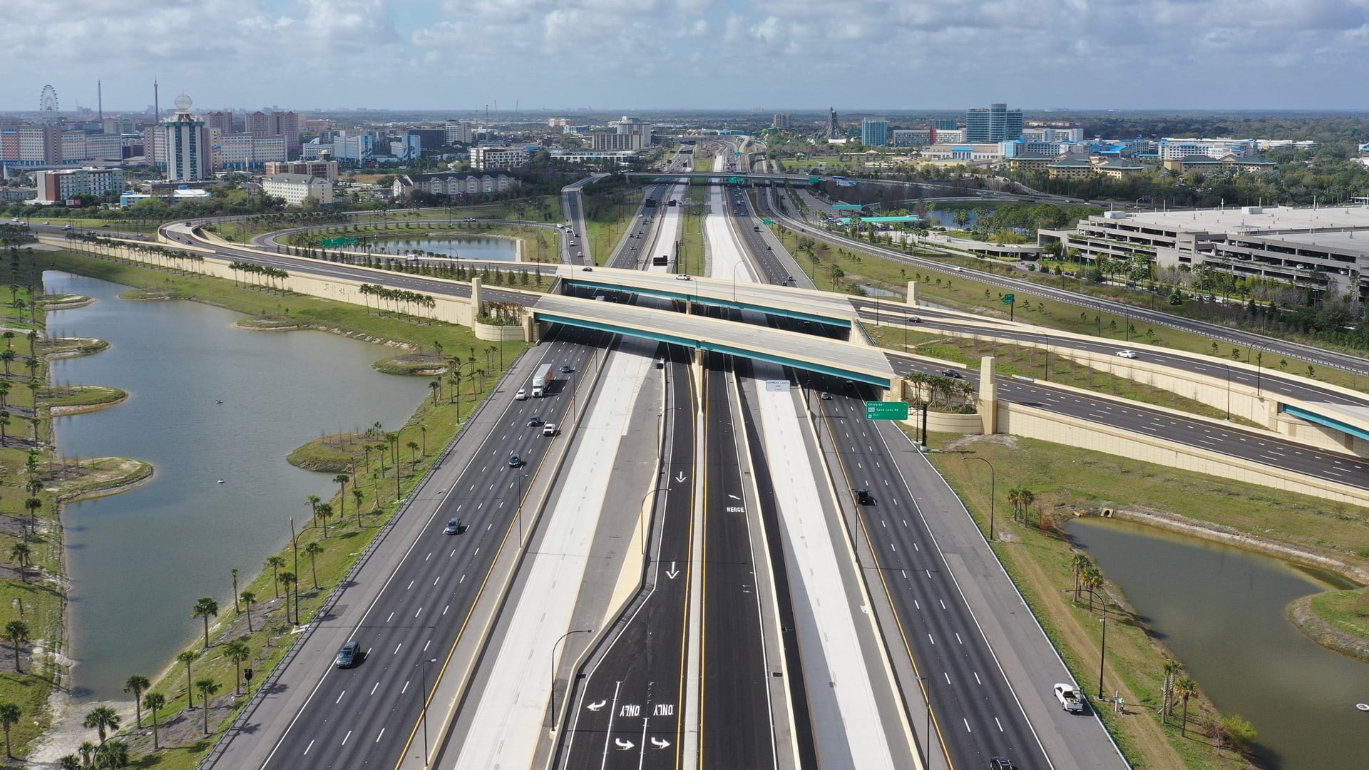 Aerial view of a modern highway intersection with surrounding urban landscape and water bodies.