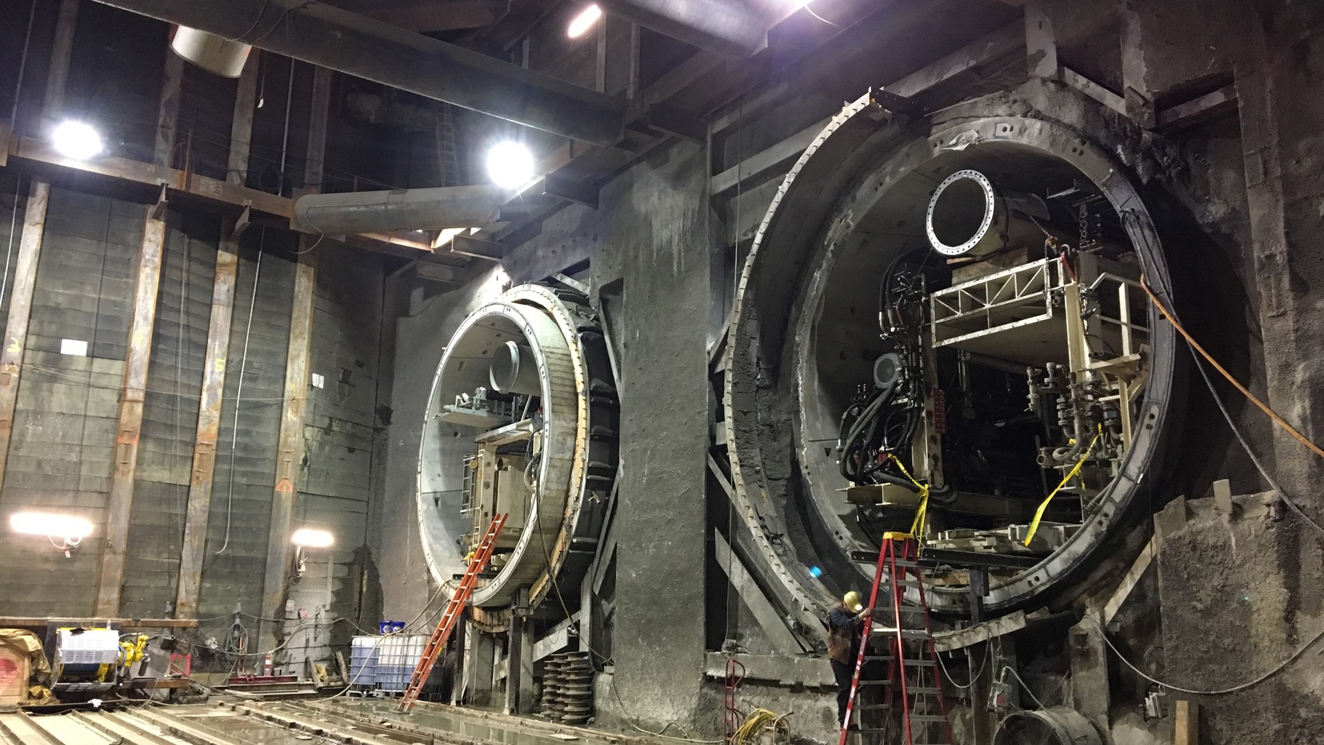 Tunnel boring machines inside an underground construction site with workers and equipment.