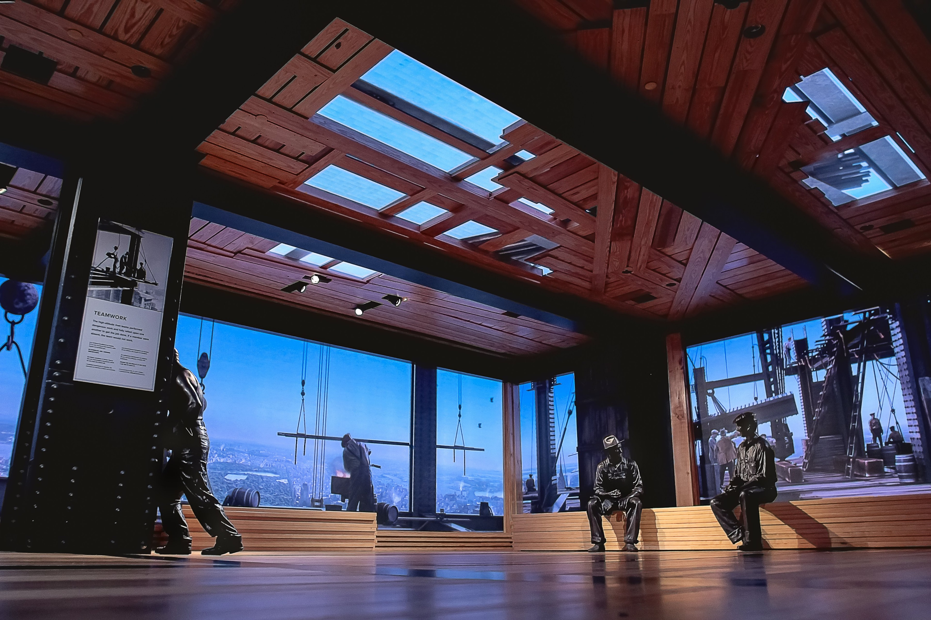 Modern wooden interior with large windows and people sitting on benches inside.