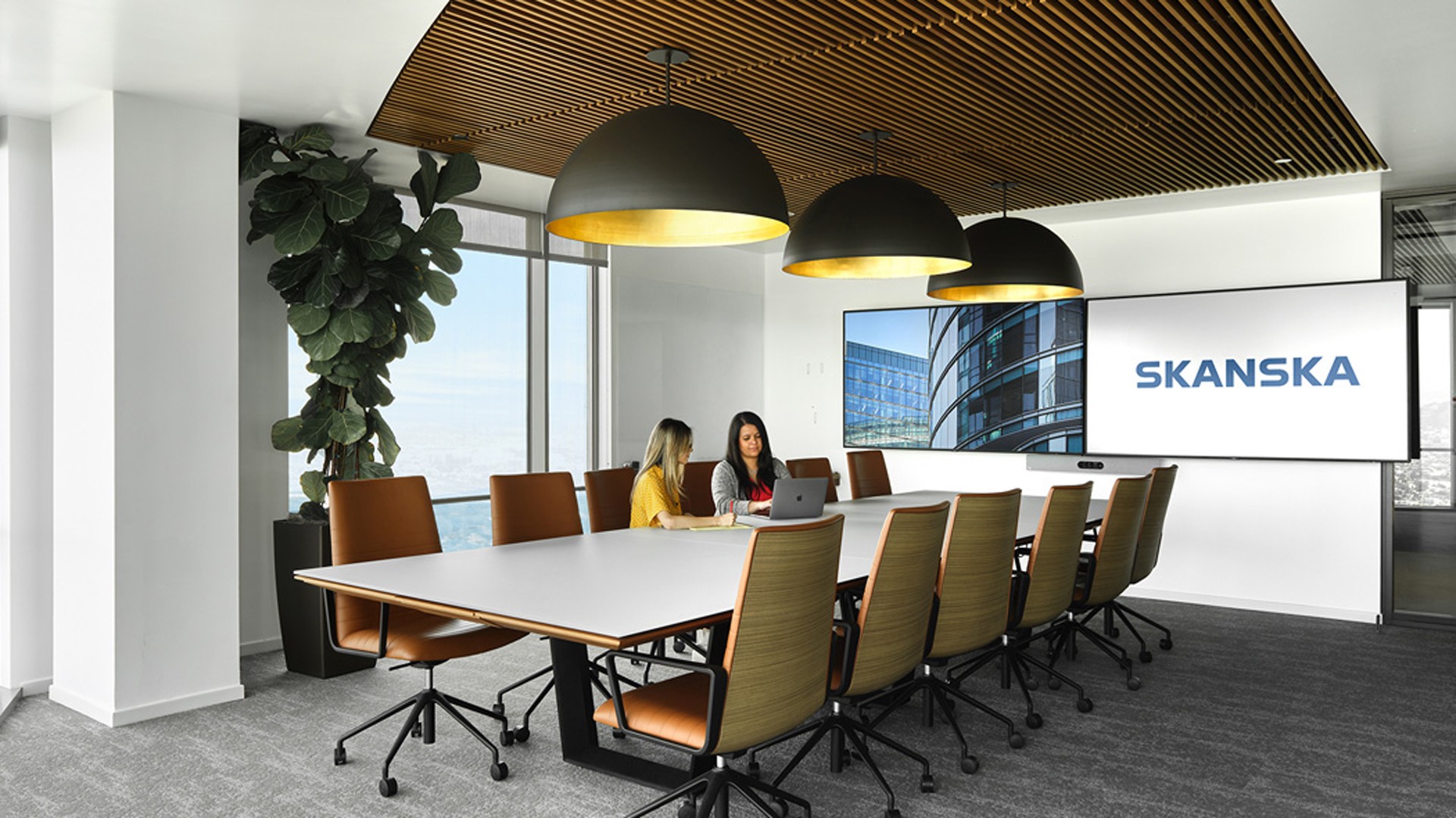 Modern Office Meeting Room with Skanska Branding Display Modern office conference room with large table, chairs, and digital screens displaying Skanska.