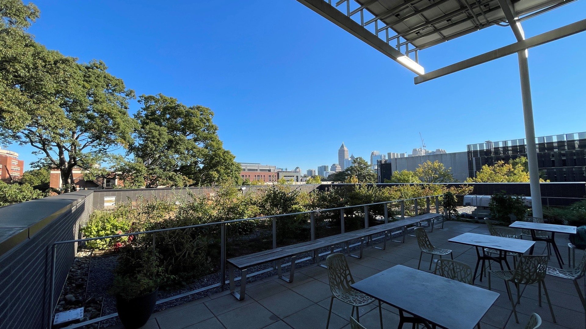 Rooftop Patio with City Skyline and Clear Blue Sky View Rooftop patio with tables, chairs, plants, and a city skyline under clear blue sky.