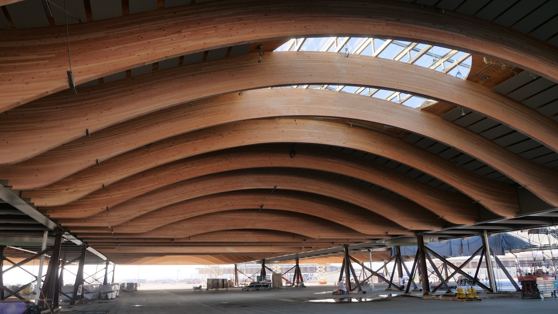 Innovative Curved Wooden Beams in Modern Architectural Design Curved wooden beams support the ceiling of a large, modern industrial building under construction.
