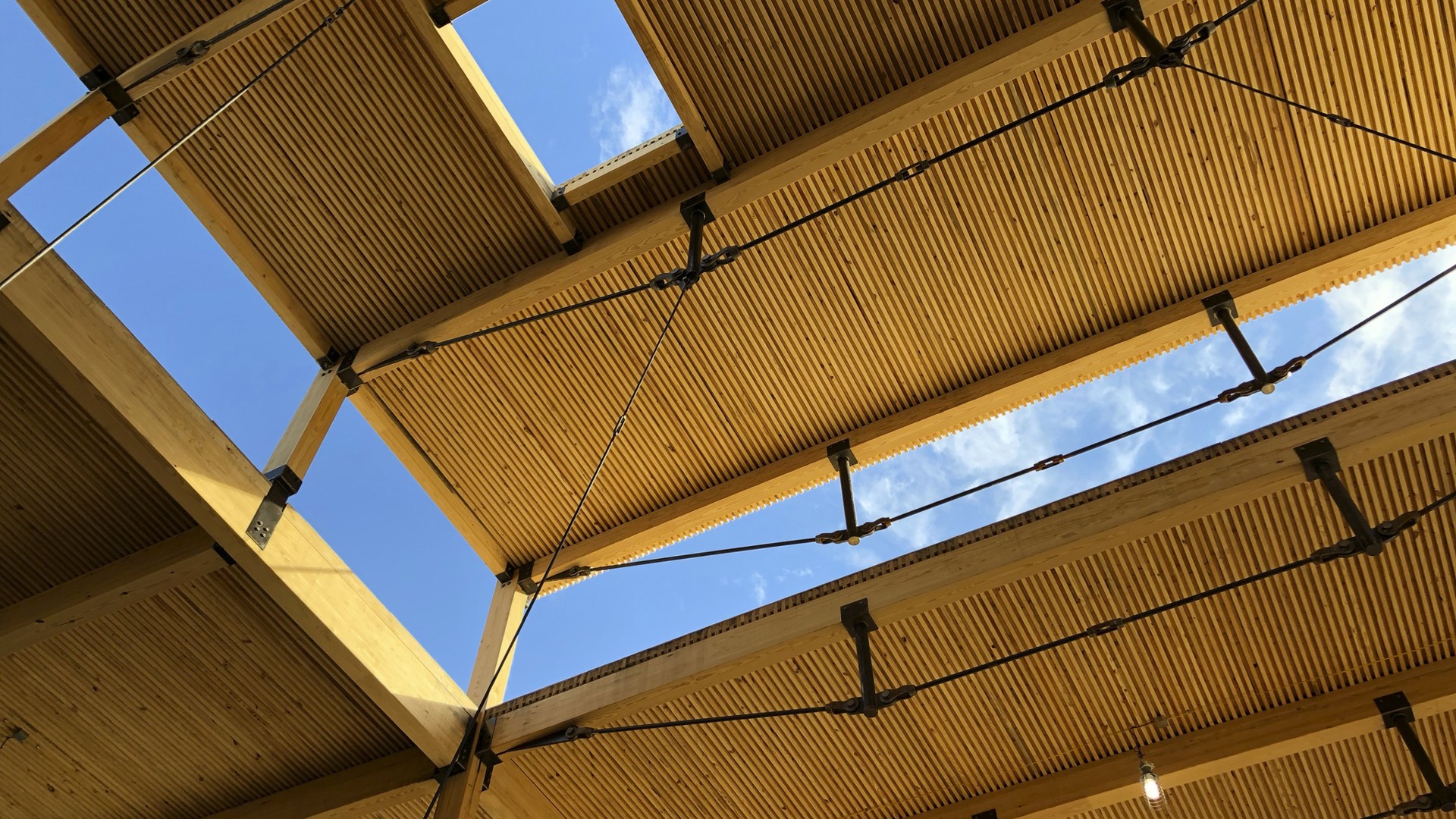 Modern wooden ceiling with open skylight and blue sky view Wooden ceiling structure with metal supports under a clear blue sky.
