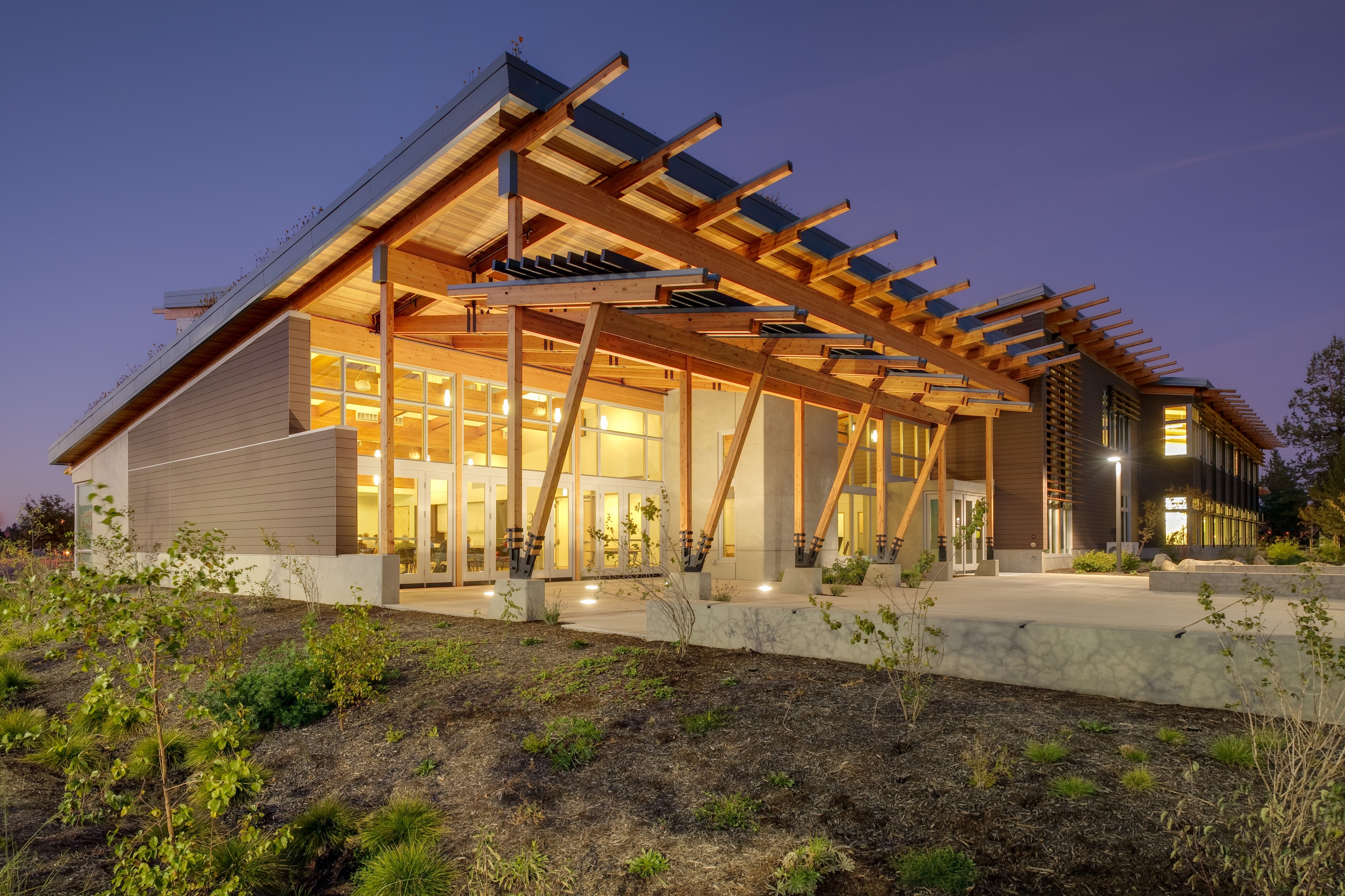 Modern building with large glass windows and wooden beams illuminated at dusk.