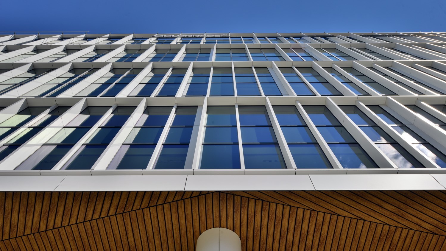Modern building facade with large glass windows and geometric patterns against a clear blue sky.