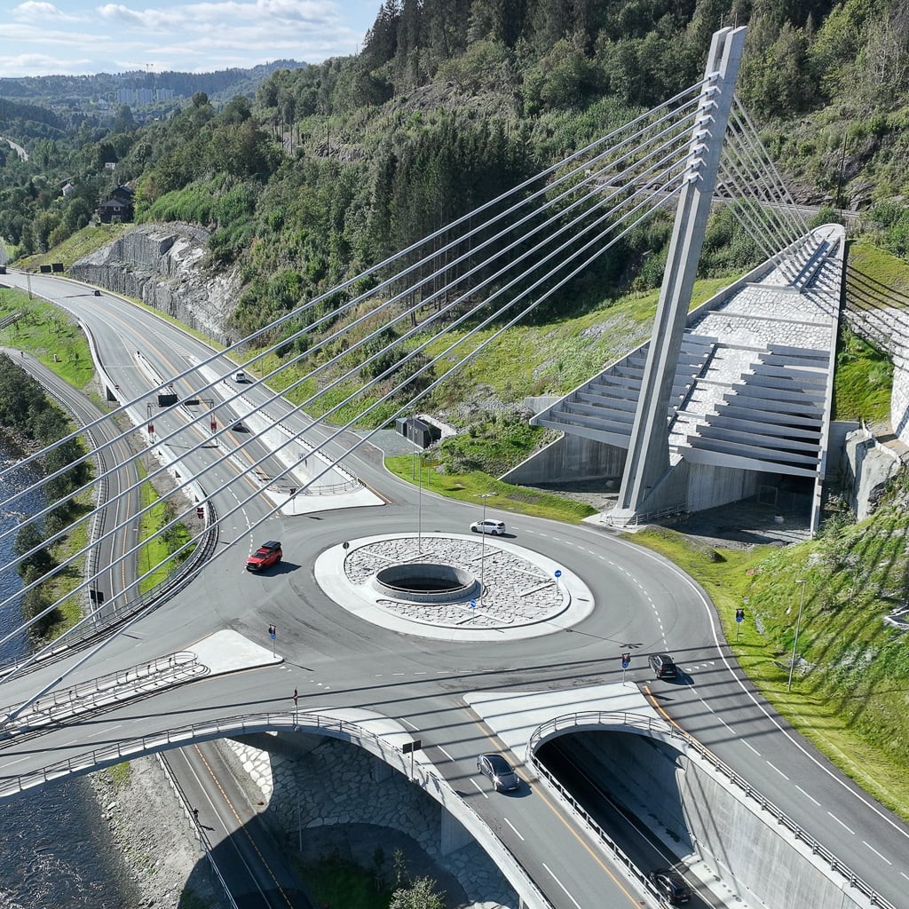 Luftfoto av en skråkabelbro med en rundkjøring plassert blant frodige, grønne åser og en vei.