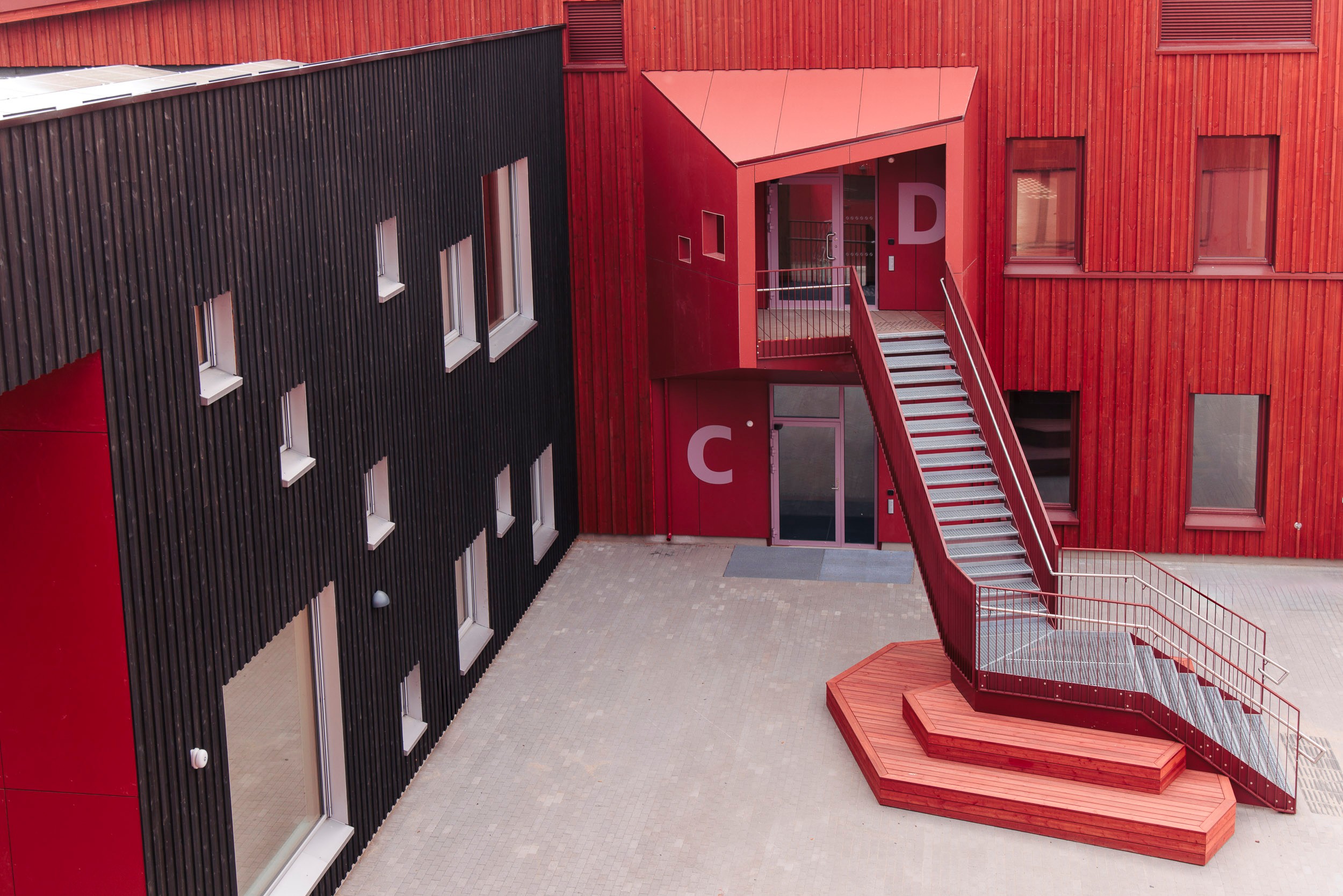 Modern red and black building exterior with geometric design and staircase leading to entrance.