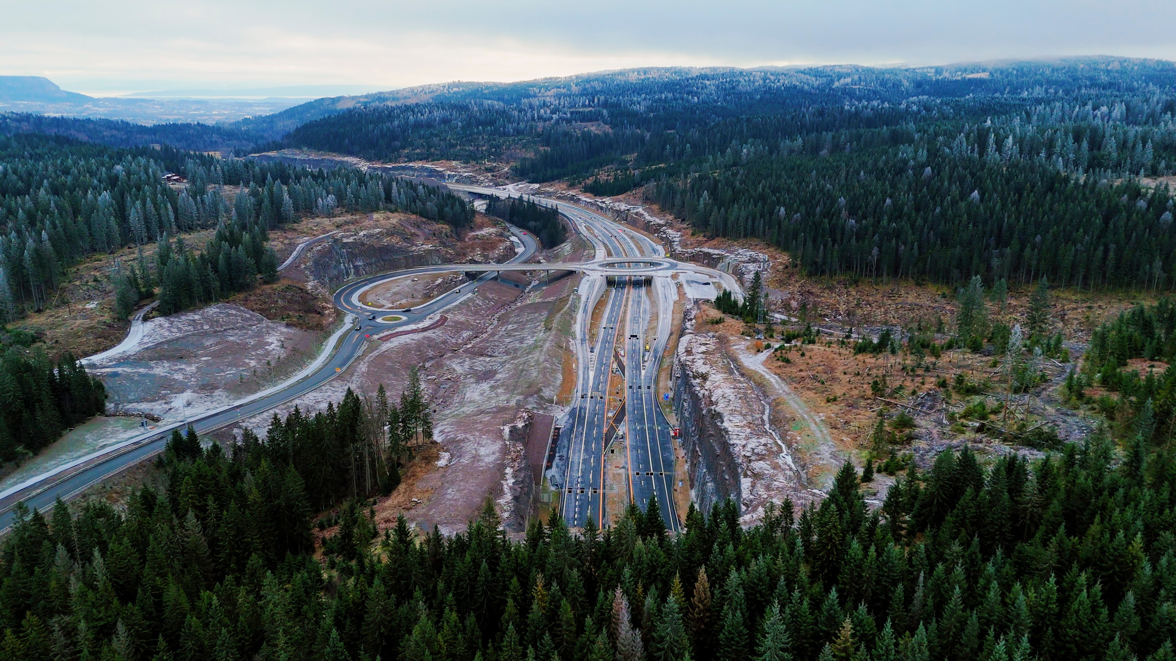 E16 Bjørum-Skaret Luftfoto av en motorveikryss omgitt av tett skog og fjellterreng.