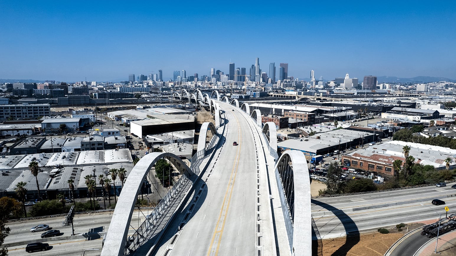 Aerial view of a modern bridge leading to a sprawling cityscape under a clear blue sky.