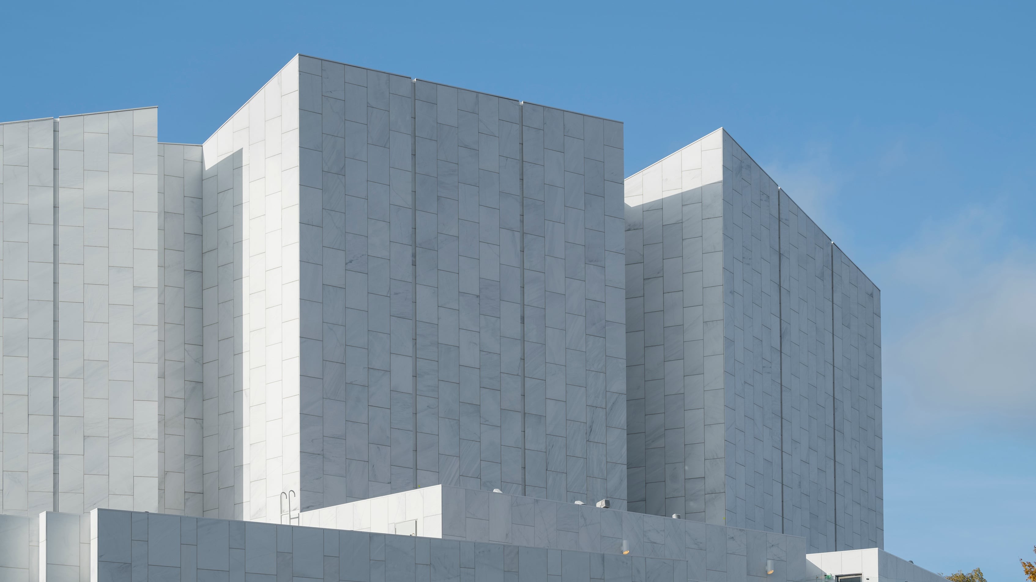 Modern building with geometric design and white stone facade under a clear blue sky.