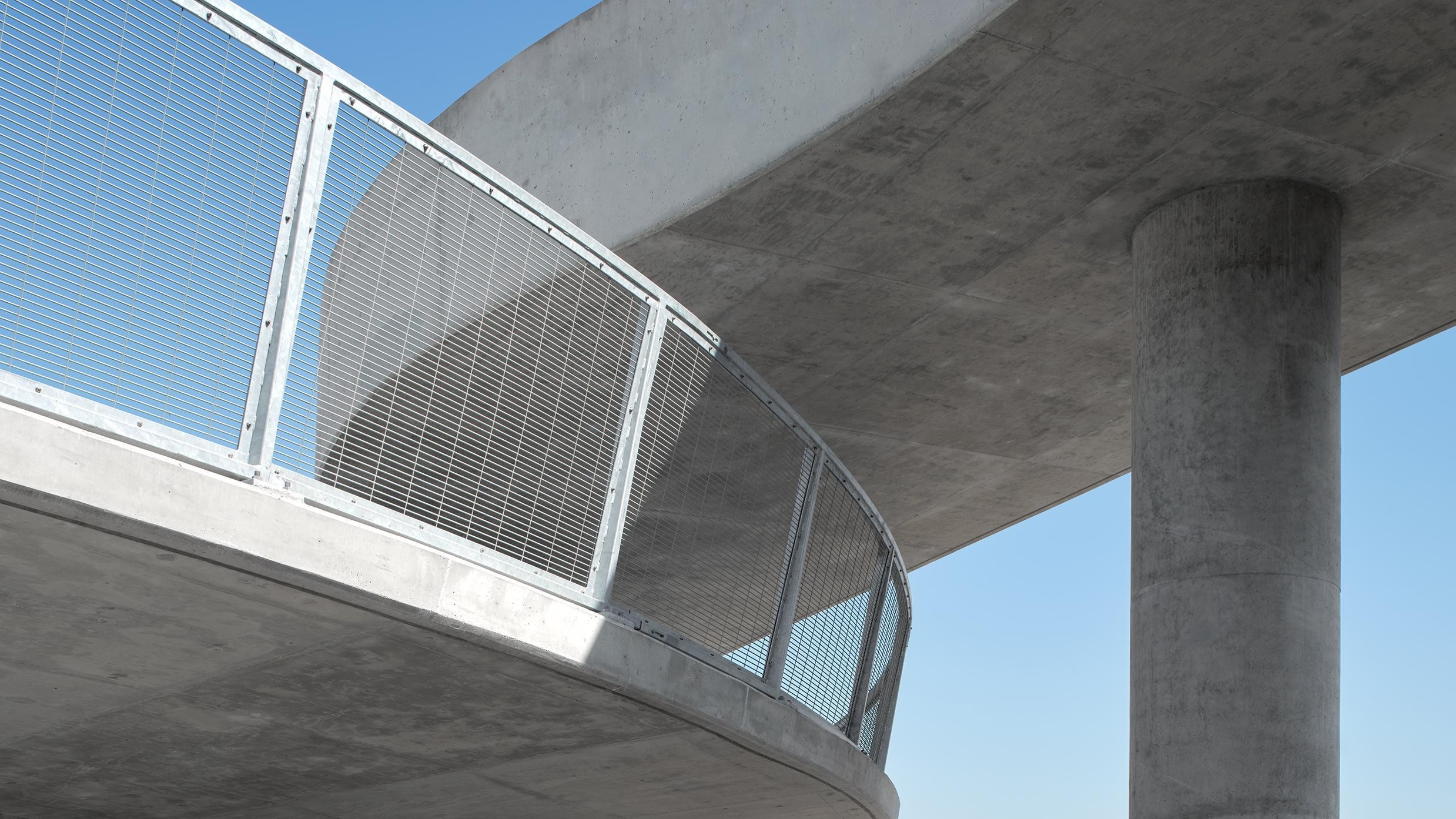 Curved concrete bridge with metal railing and clear blue sky background.