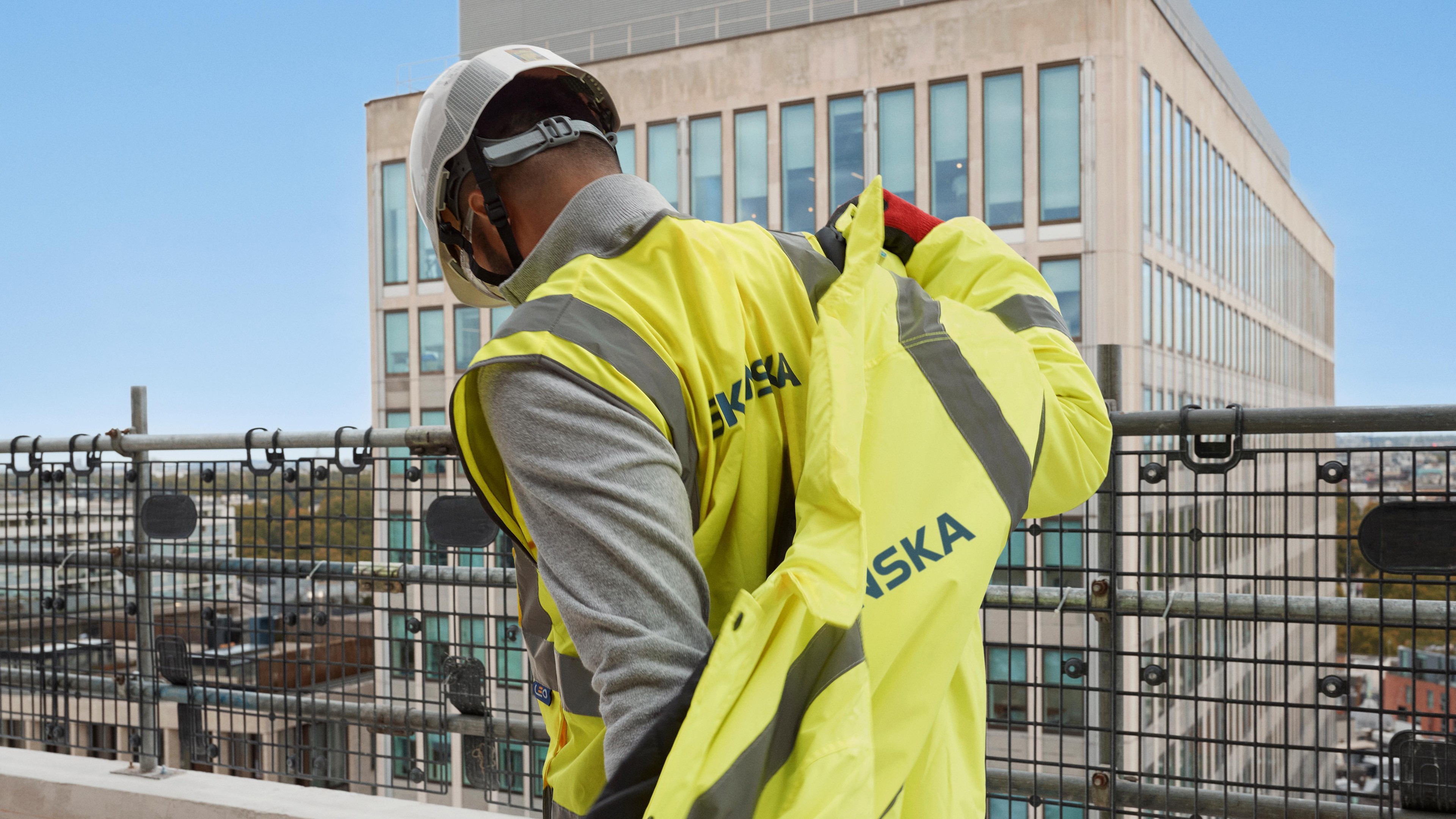 Worker wearing a yellow reflective safety vest putting on a jacket on a construction site.