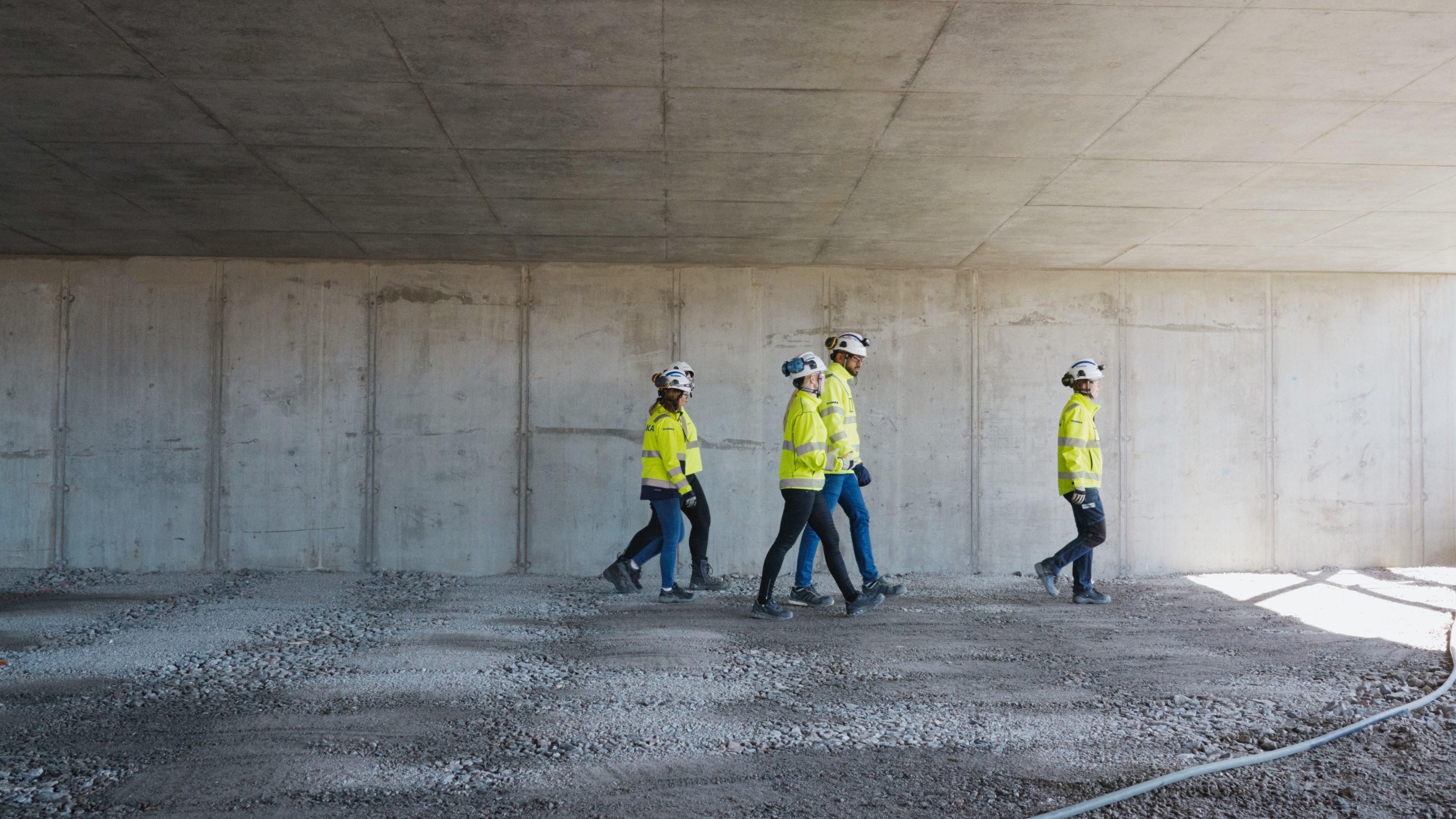Construction workers in safety gear walking inside an unfinished concrete building site.