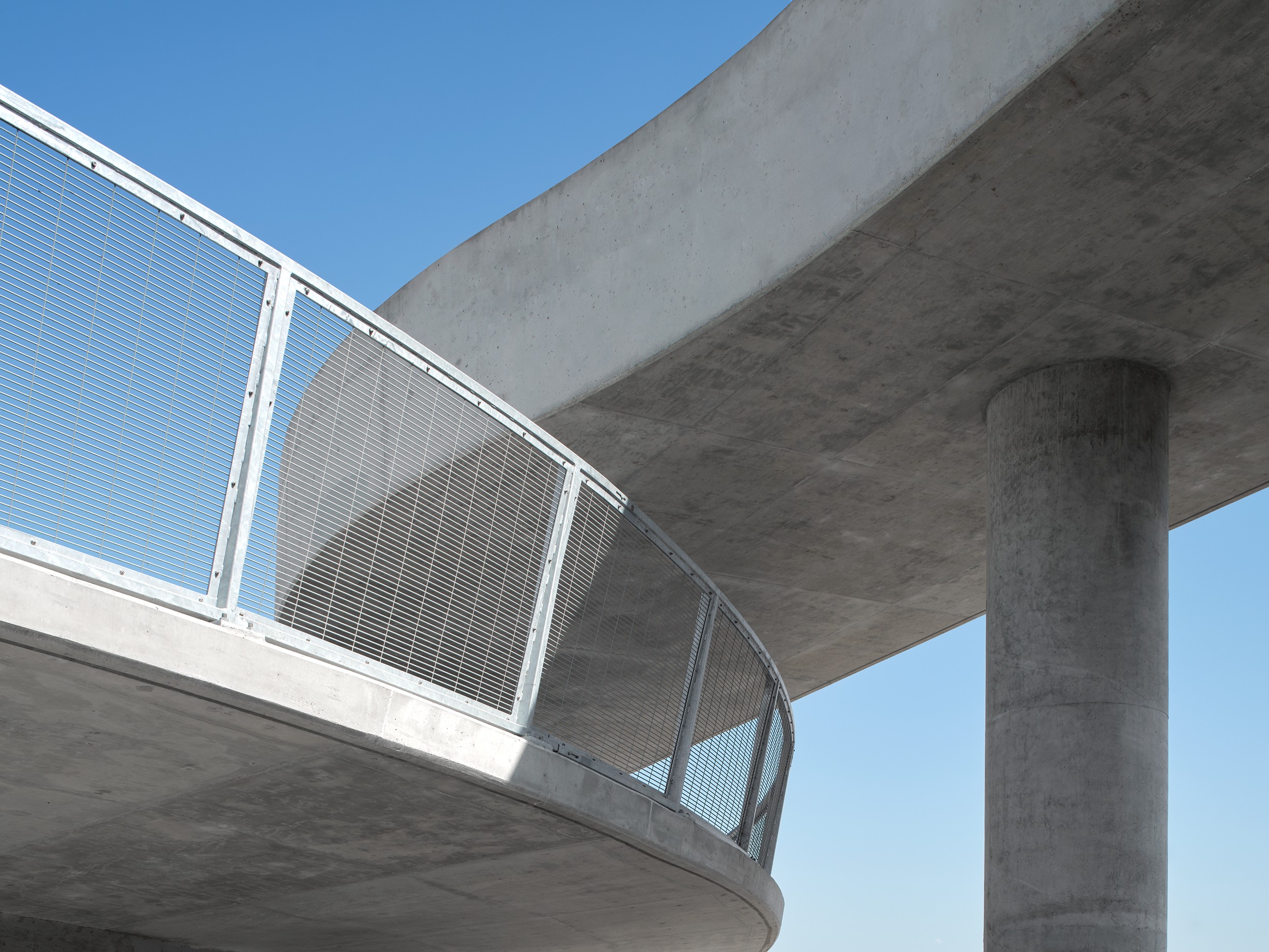 Curved concrete bridge with metal railing against a clear blue sky background.