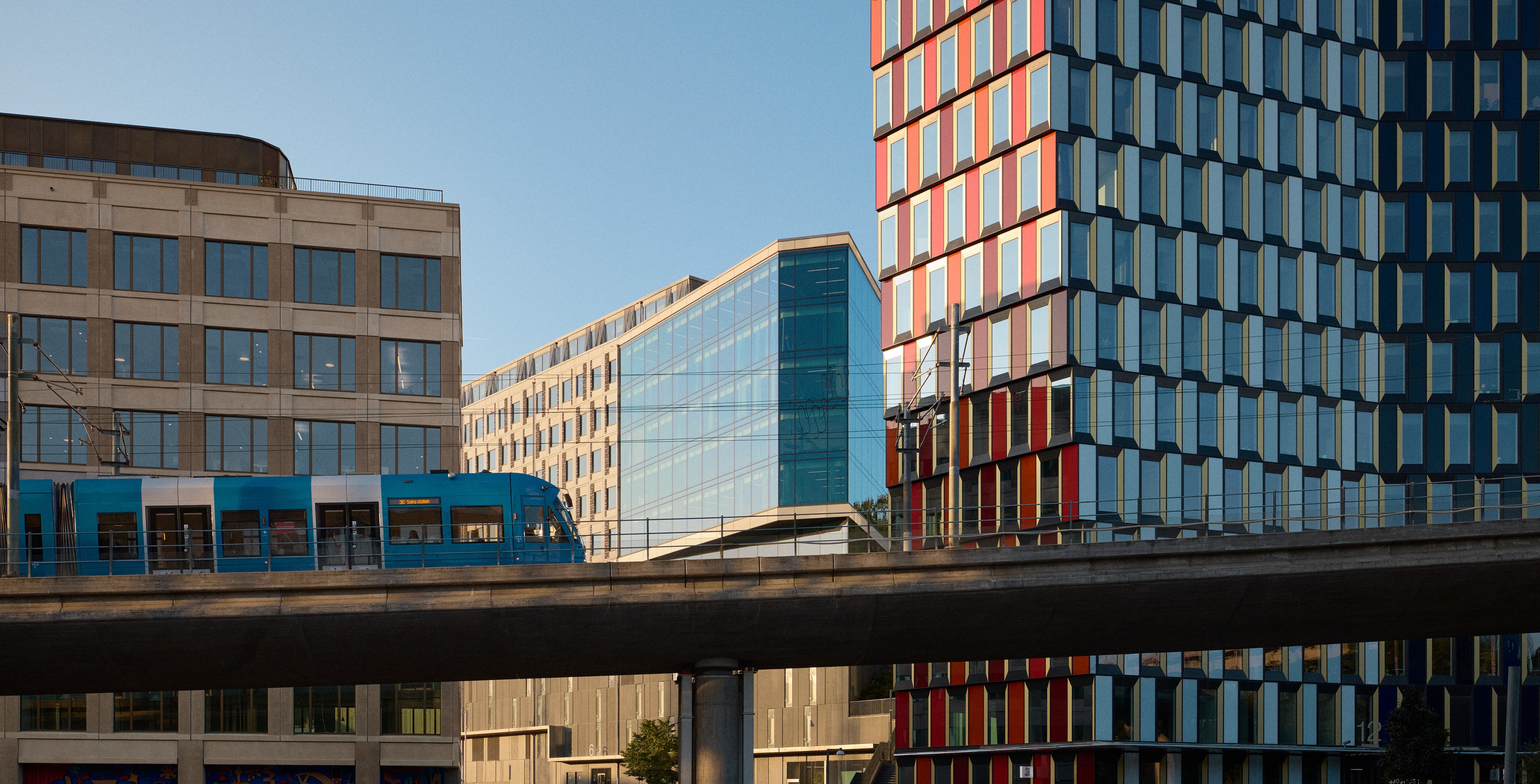 Modern cityscape with a blue tram on an elevated track between glass office buildings.