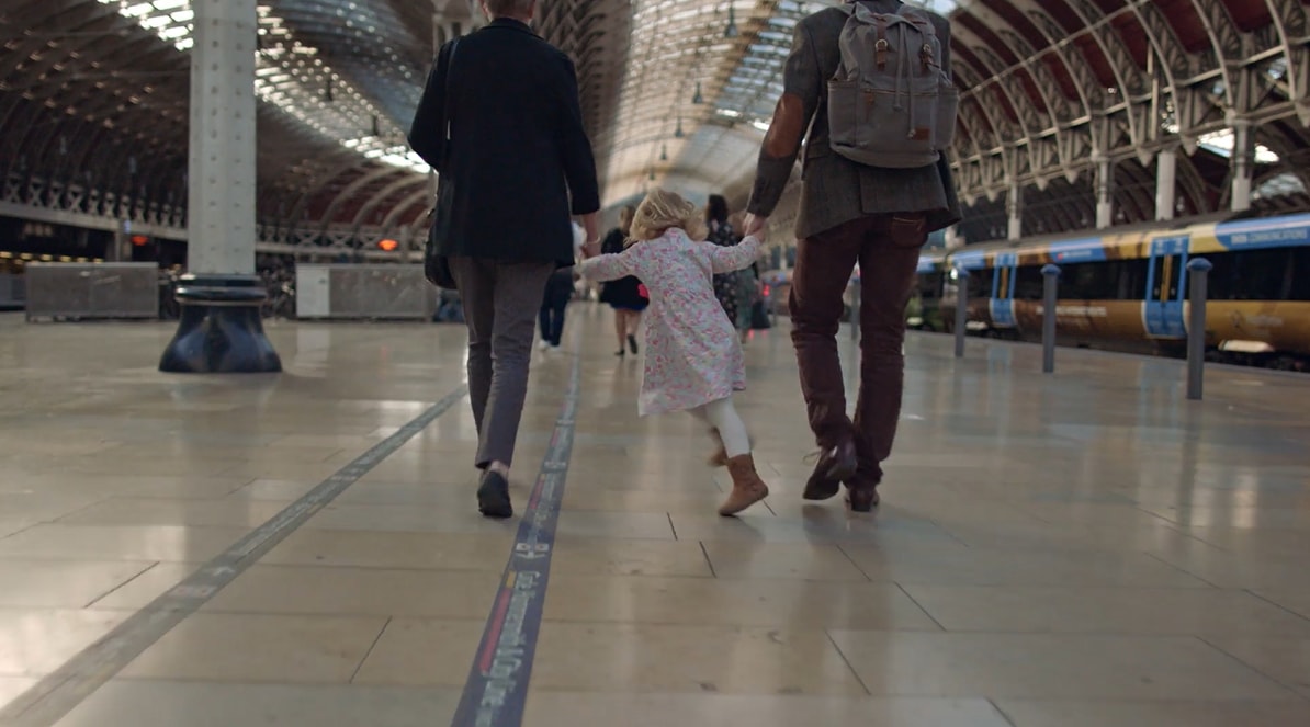 A child holding hands with two adults walking in a spacious train station.