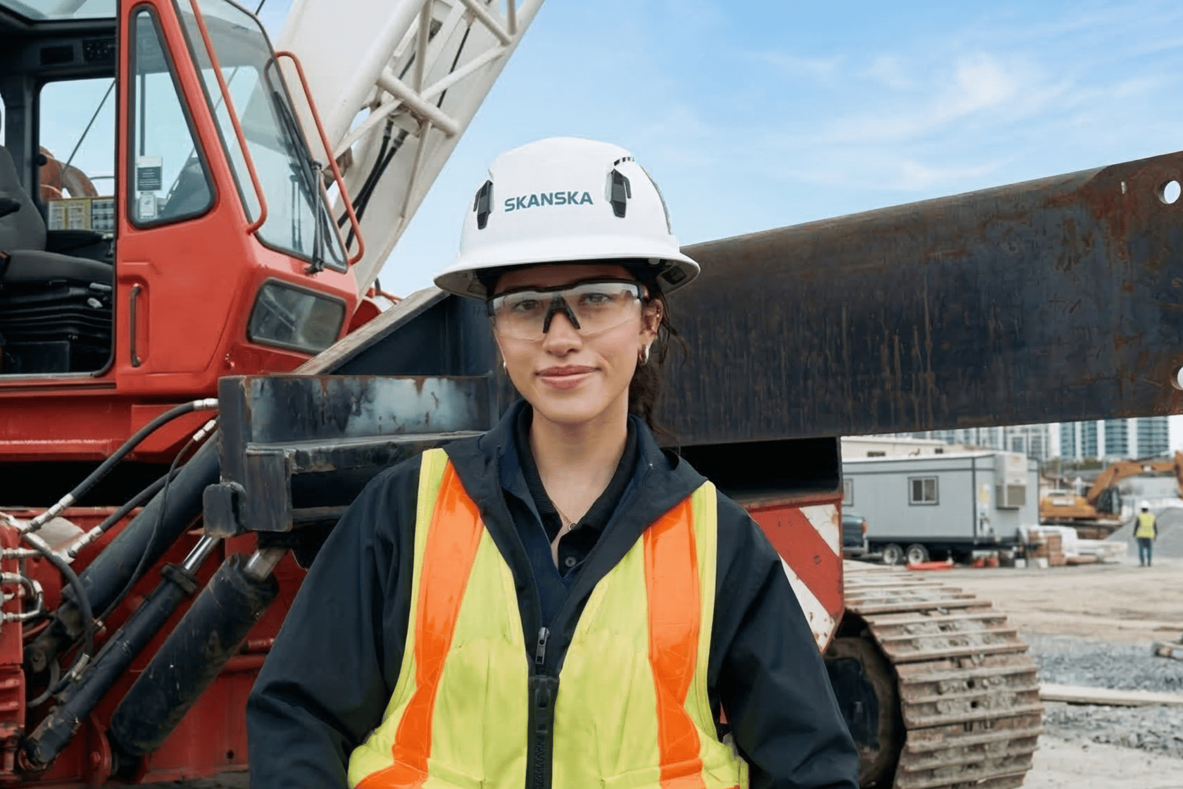 Construction worker in safety gear standing in front of a red crane at a job site.