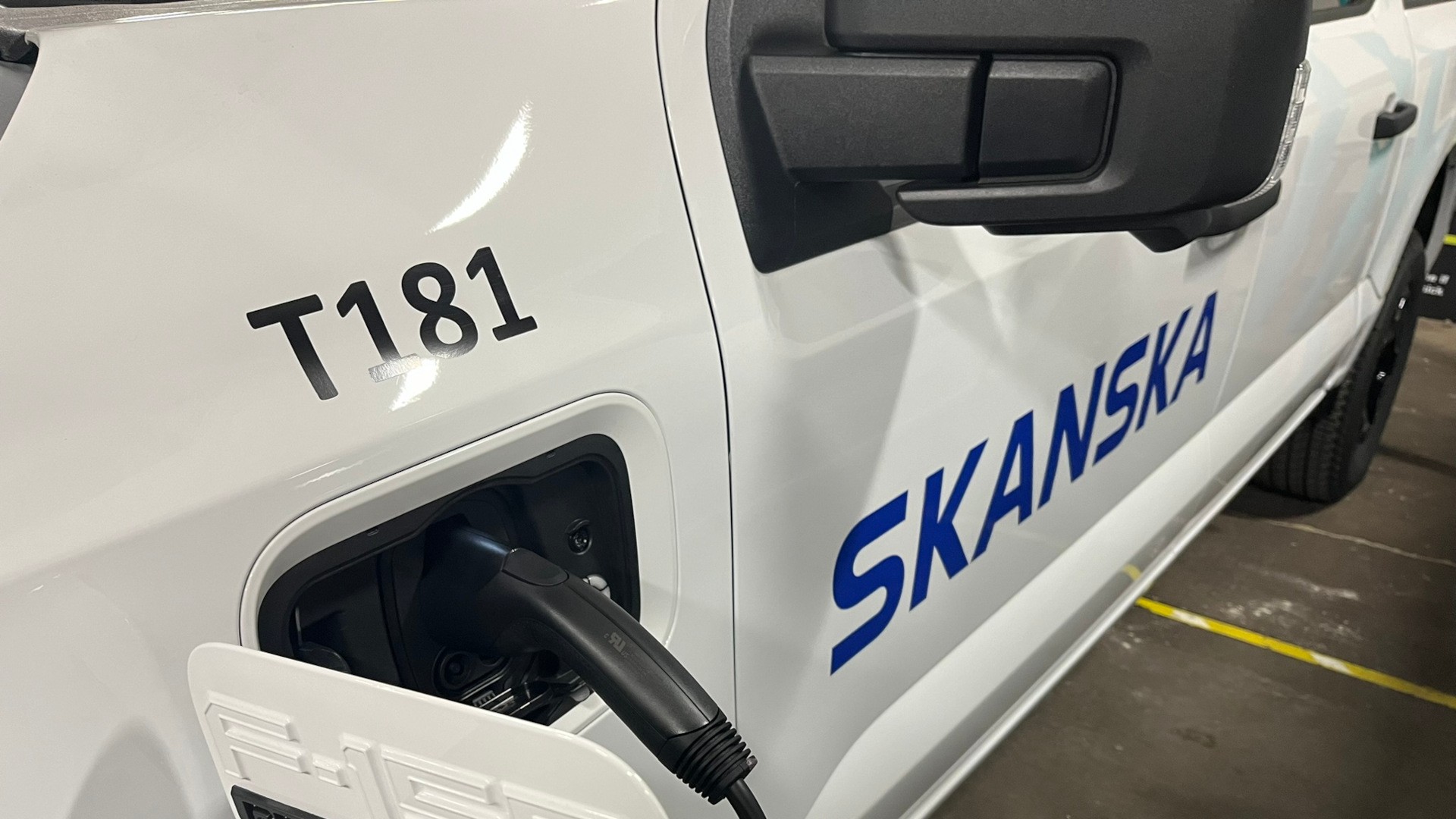 Electric vehicle charging with Skanska branding and T181 identifier on the side.