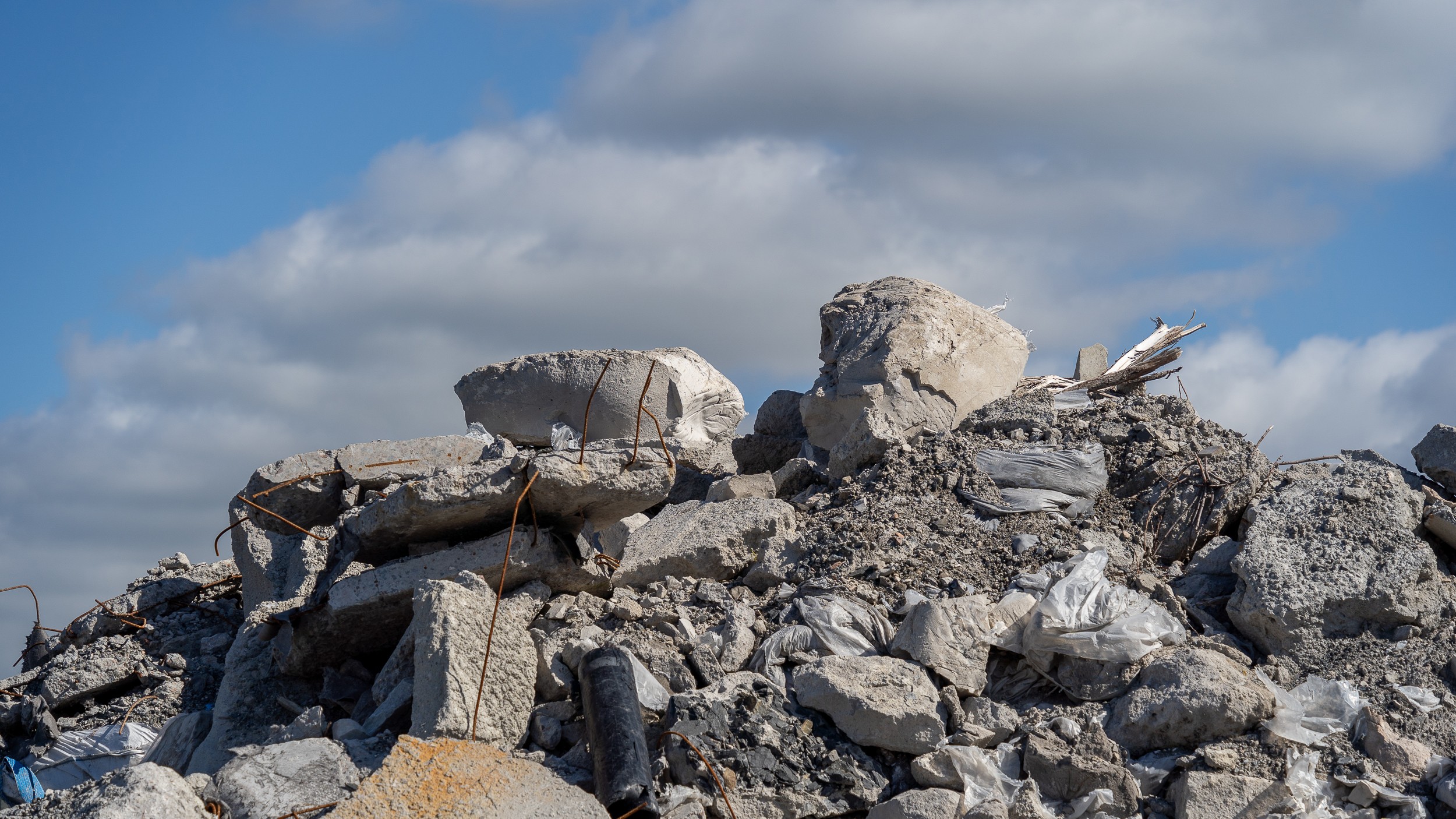 Construction Debris Under Blue Sky: A Dramatic Perspective Pile of construction debris under a cloudy sky, featuring concrete chunks and scattered rubble.