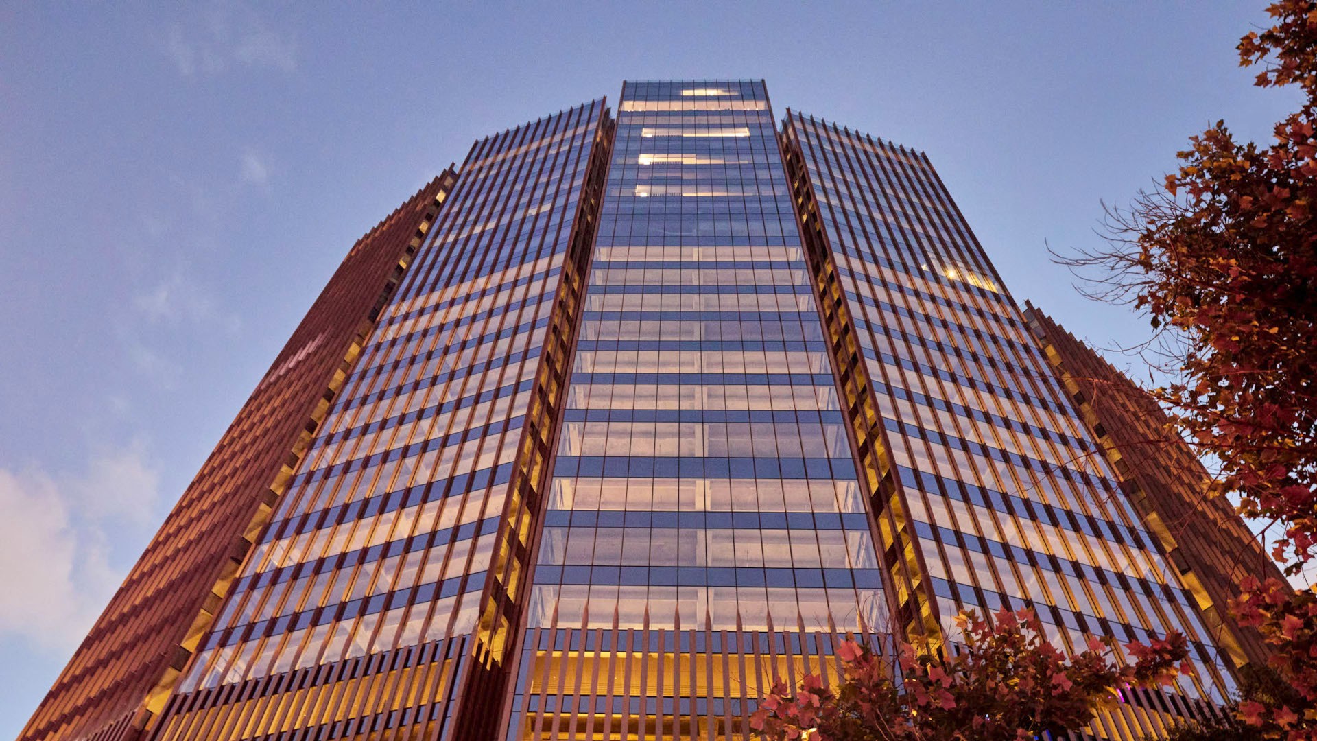 Tall modern glass building with reflective windows against a twilight sky, viewed from below.