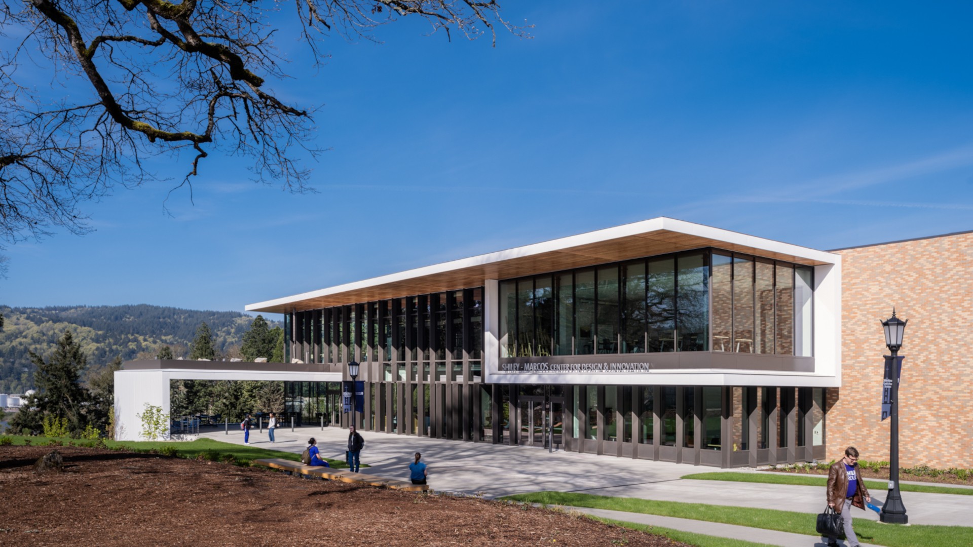 Modern educational building with large glass windows, surrounded by greenery under a clear blue sky.